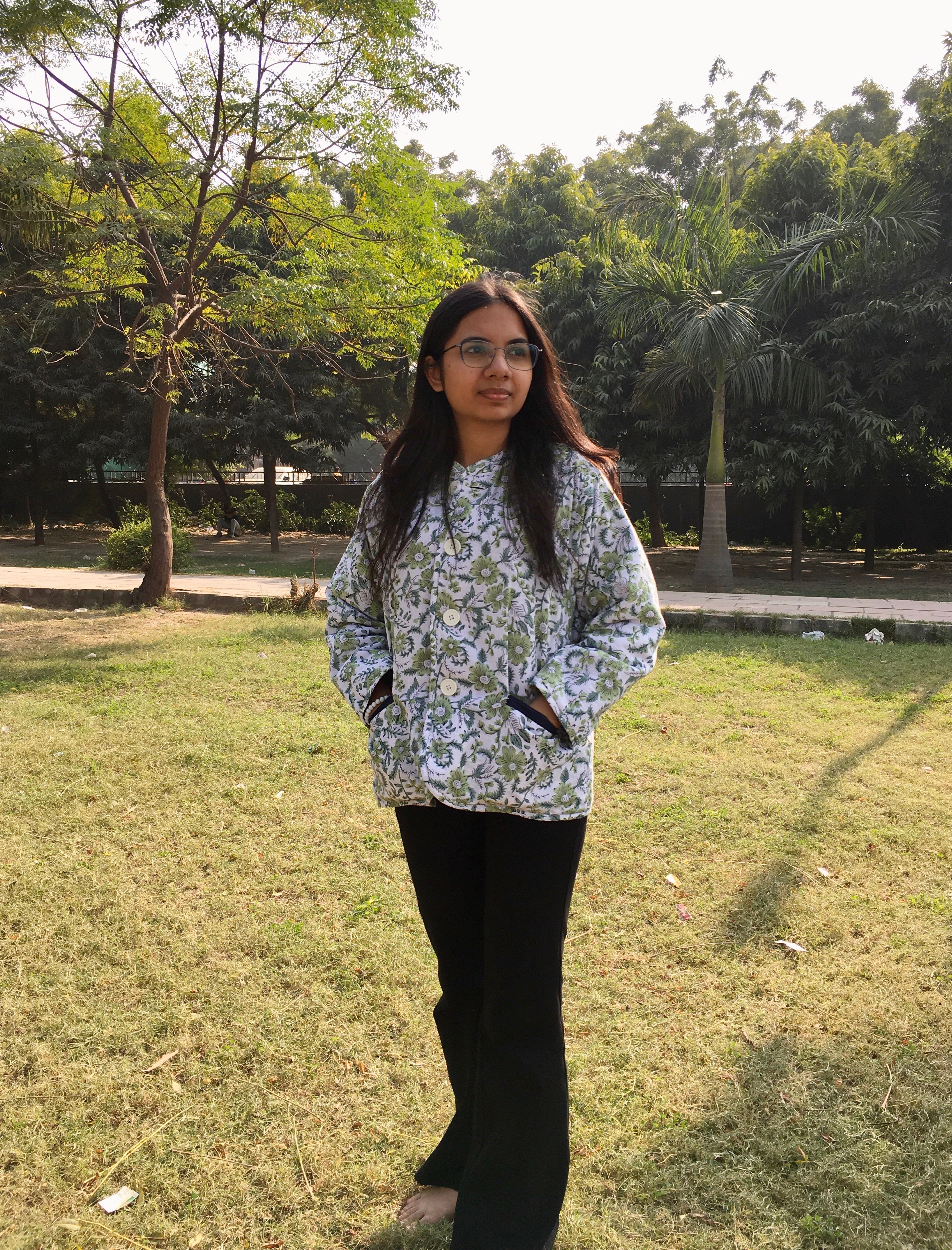 Woman wearing a reversible floral and hand-block printed jacket in an outdoor park.