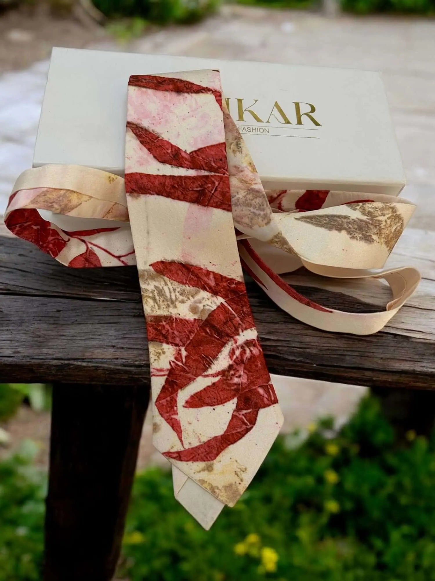 Red and white patterned silk tie with a box labeled 'Vikar' on a wooden surface outdoors.