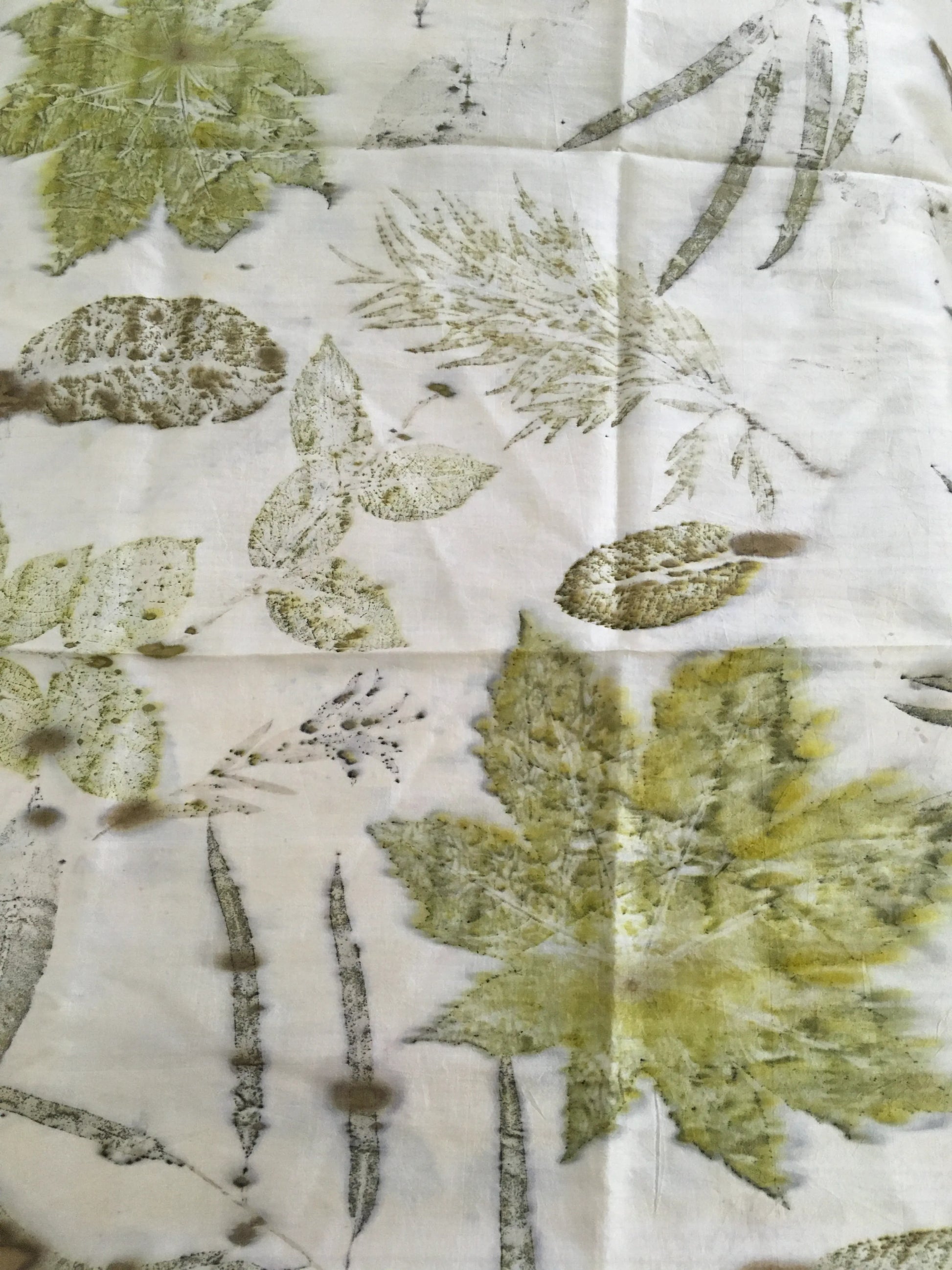 Handcrafted pure silk scarf featuring eco-printed green botanical leaves and natural foliage patterns on a white silk background using sustainable eco-printing techniques.