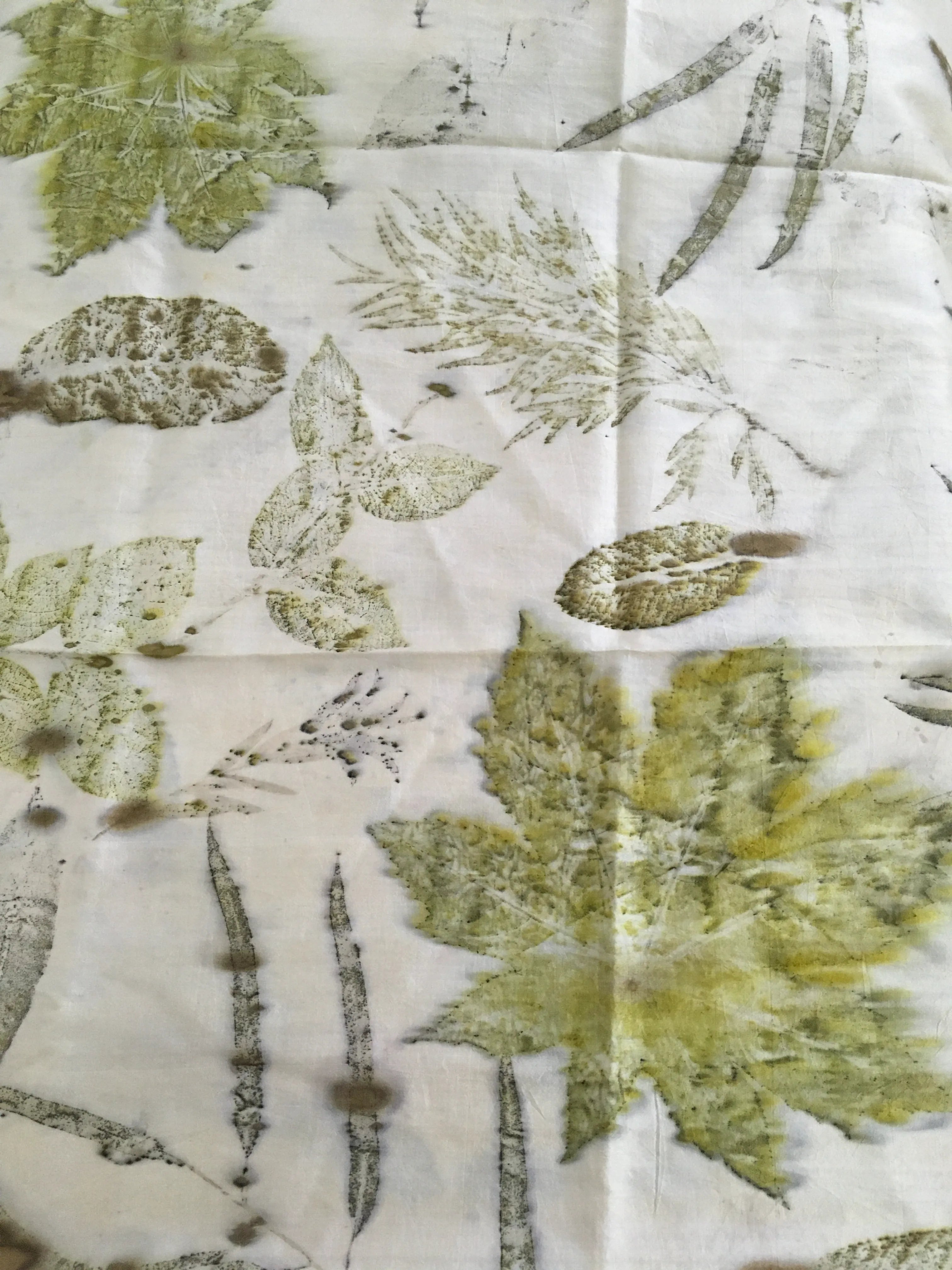 Handcrafted pure silk scarf featuring eco-printed green botanical leaves and natural foliage patterns on a white silk background using sustainable eco-printing techniques.