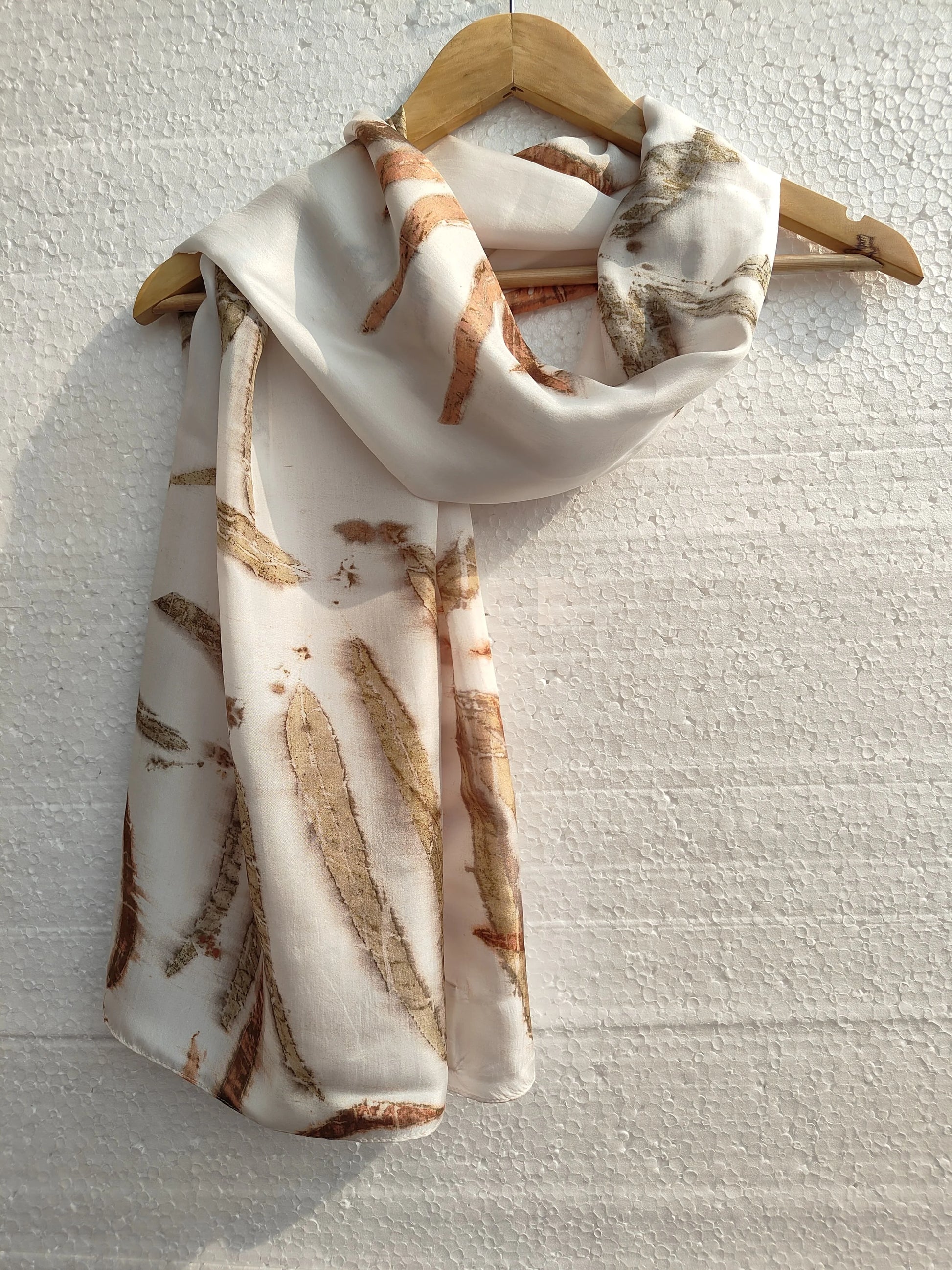 Neatly folded Camellia Ecoprinted Pure Silk Scarf on a wooden hanger against a light textured background