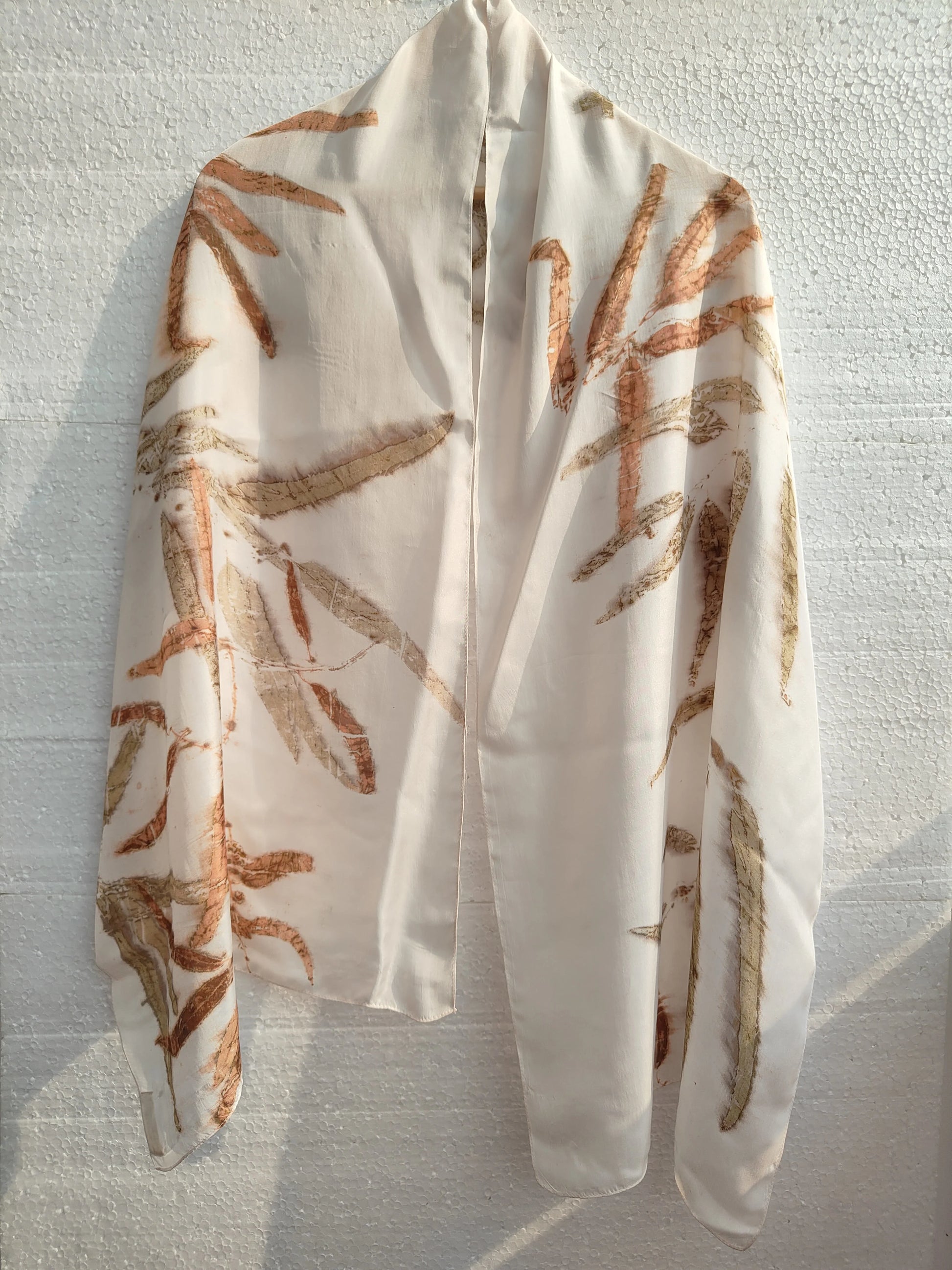 White silk scarf with brown Eucalyptus leaf pattern on a textured white background wall of kokikar