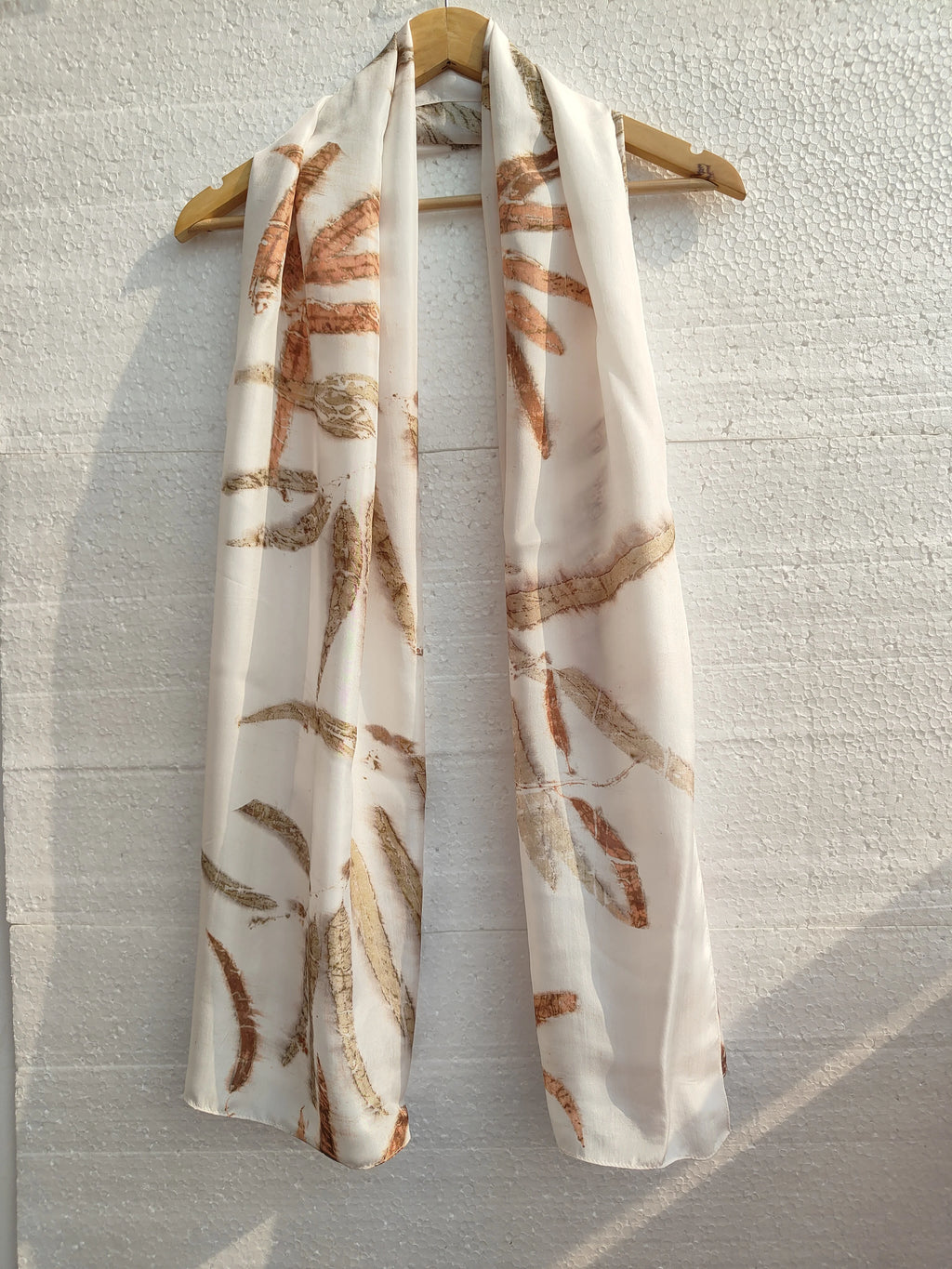 Silk Scarf with Eucalyptus leaf pattern on a wooden hanger against a light gray wall