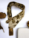 Camouflage-patterned tie on a white background with dried leaves.