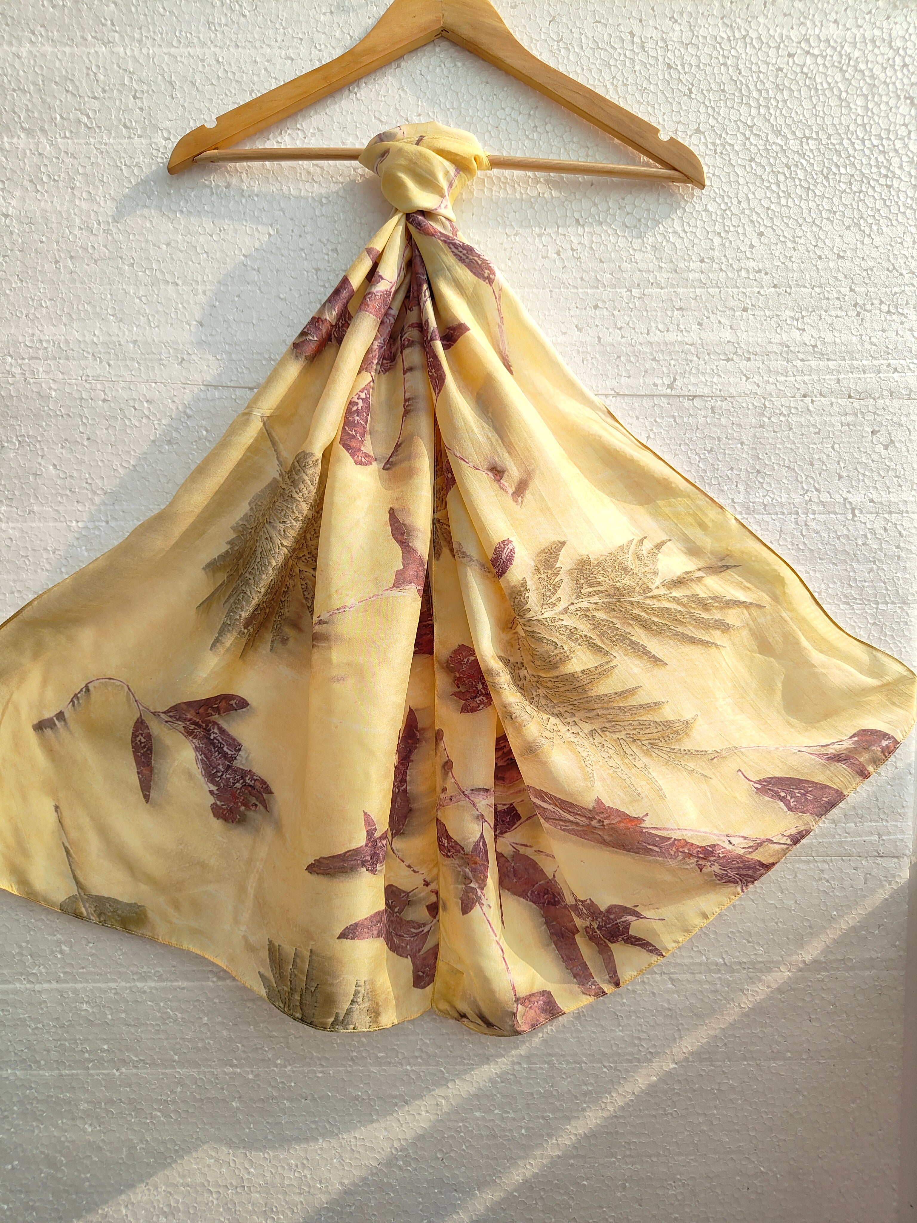 A hanging yellow scarf with ecoprinted leaves