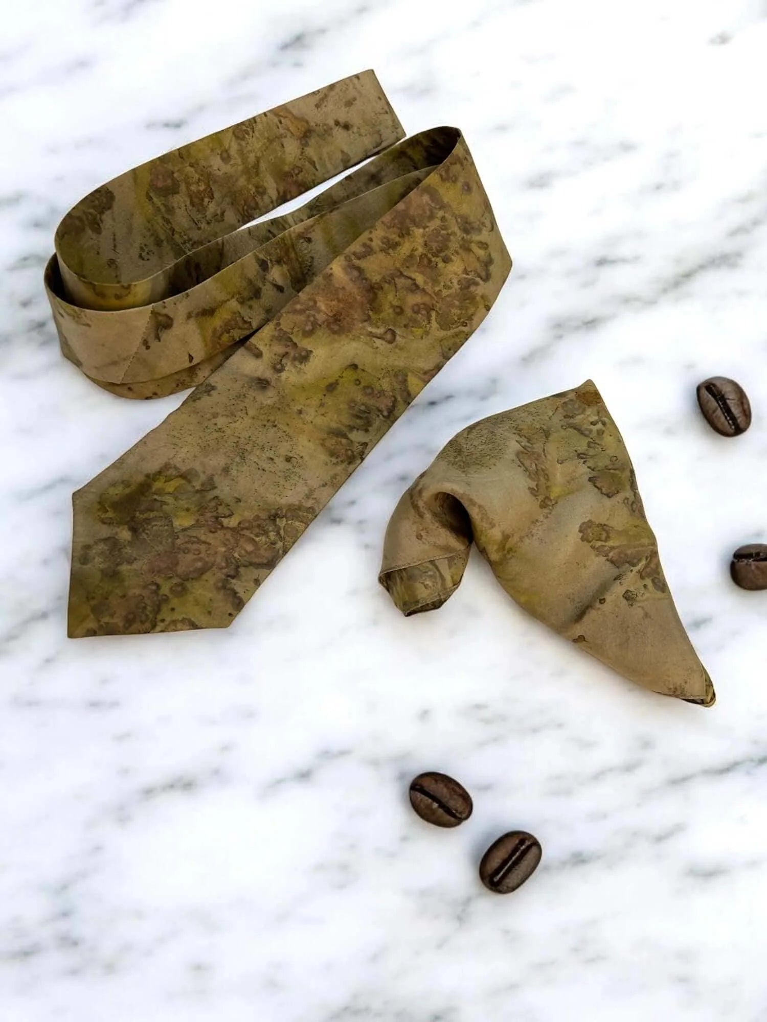 Brown patterned tie and bow tie on a marble surface with coffee beans.