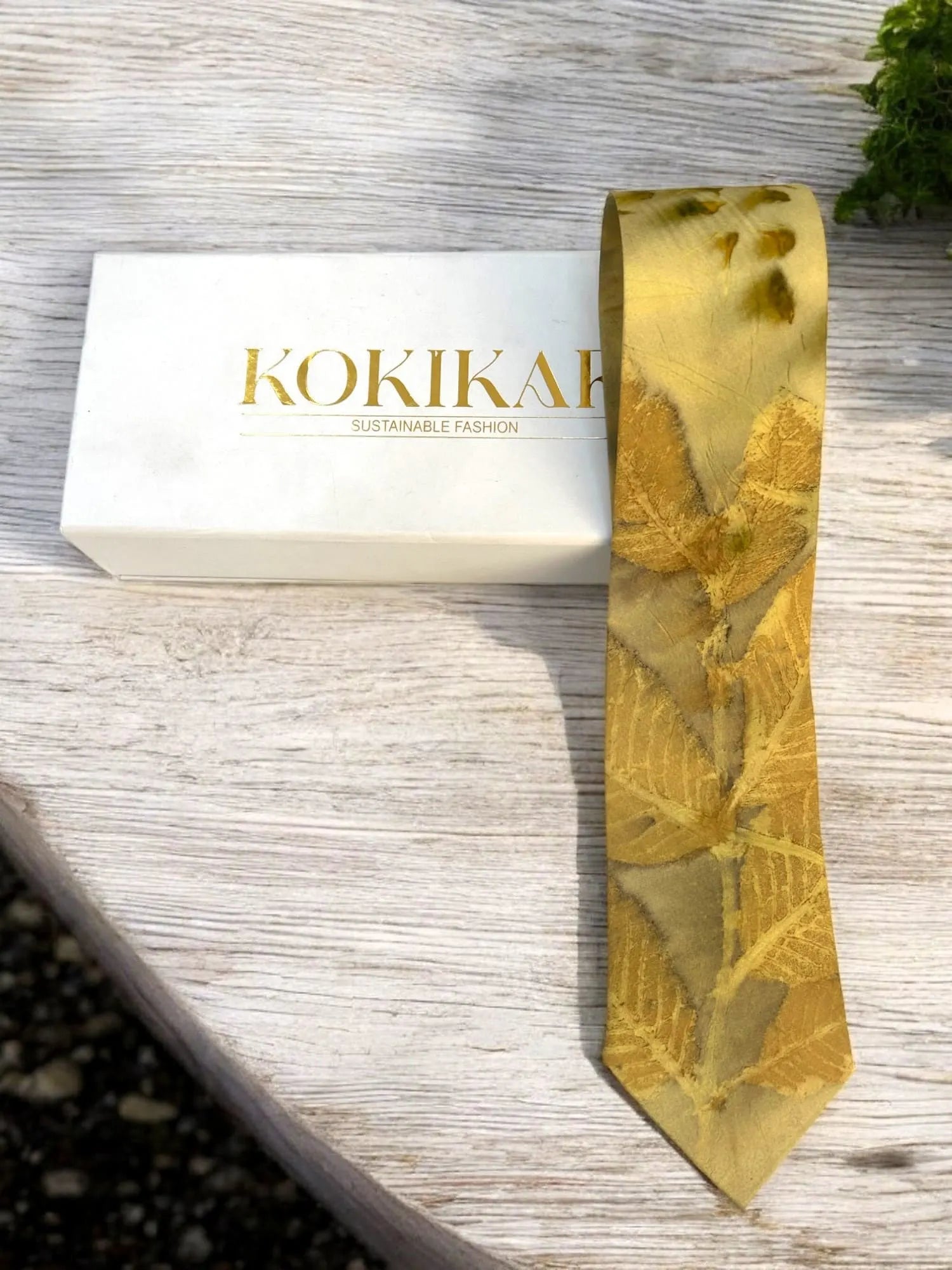 Gold tie with a pattern on a wooden surface next to a white box with 'KOKIKAR' branding.