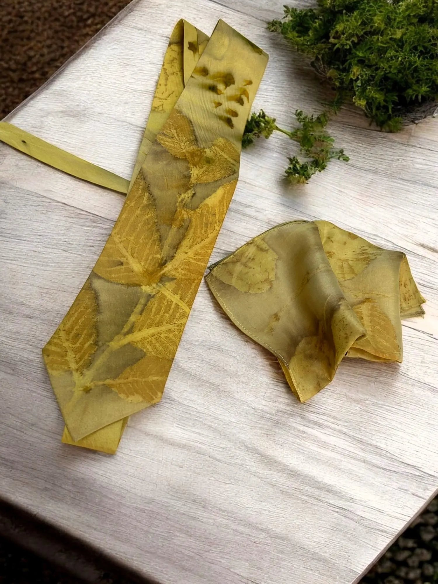 Green leaf-patterned tie on a wooden surface with greenery.