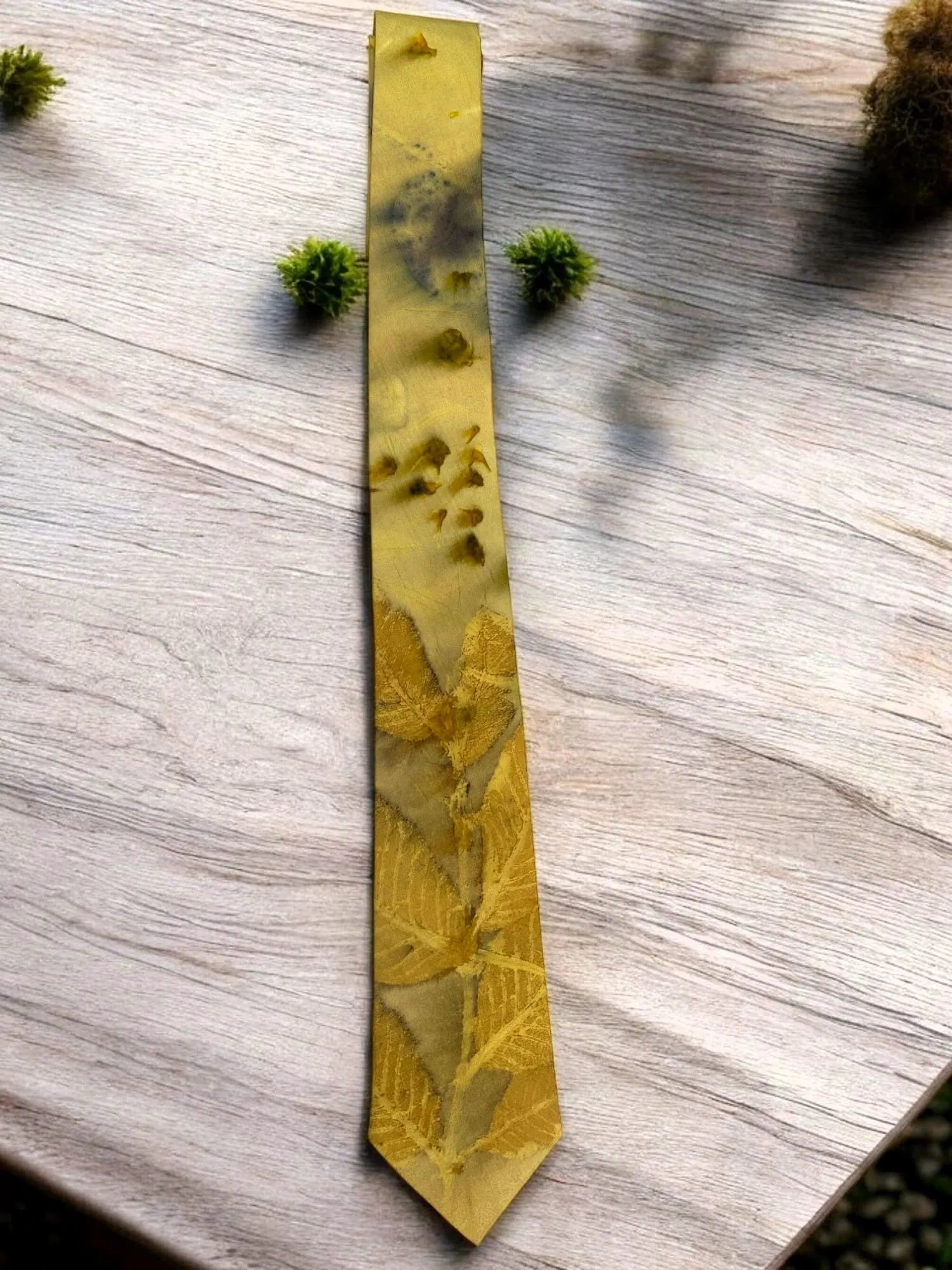 Gold tie with nature-themed pattern on a wooden surface