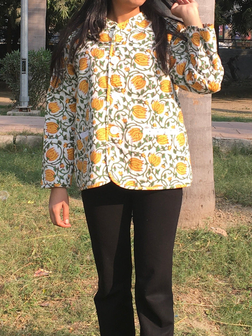women wearing a floral reversible jacket and black pants standing outdoors with trees in the background