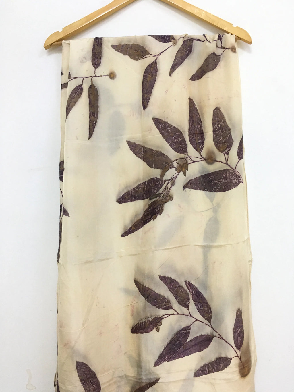Logwood Eucalyptus Eco Printed Pure Silk Scarf with leaf pattern hanging on a wooden hanger against a white background