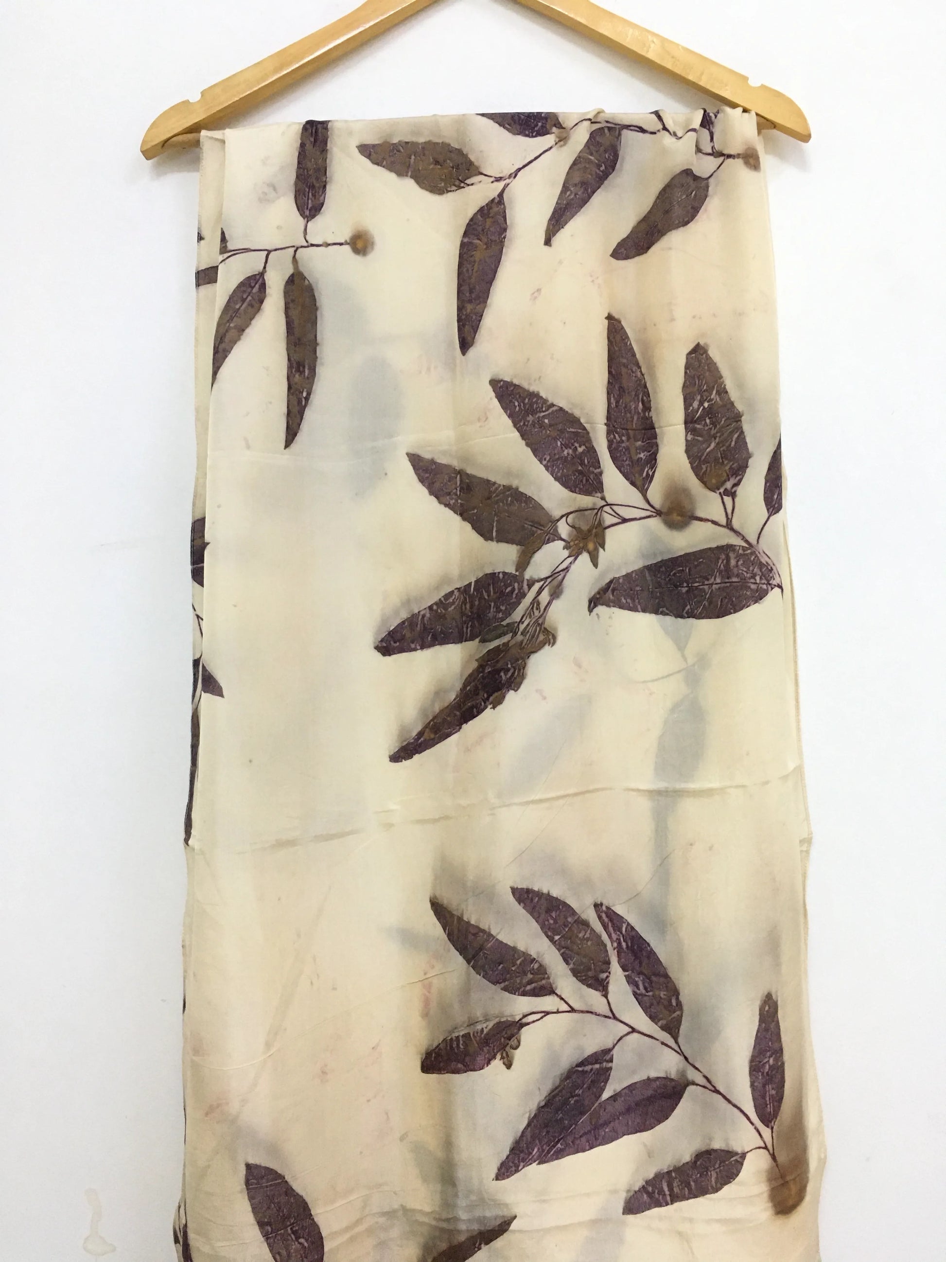 Logwood Eucalyptus Eco Printed Pure Silk Scarf with leaf pattern hanging on a wooden hanger against a white background