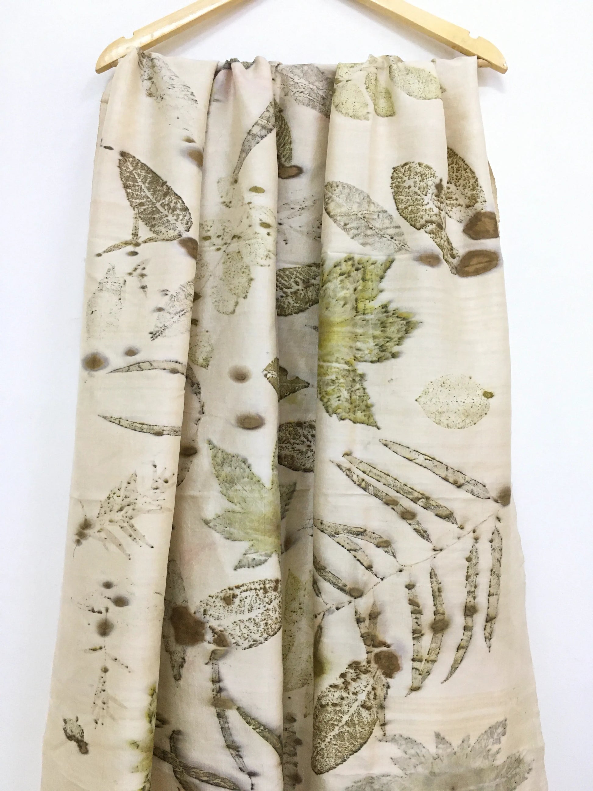 Botanical Eco Printed Pure Silk Scarf with leaf pattern hanging on a wooden hanger against a white background