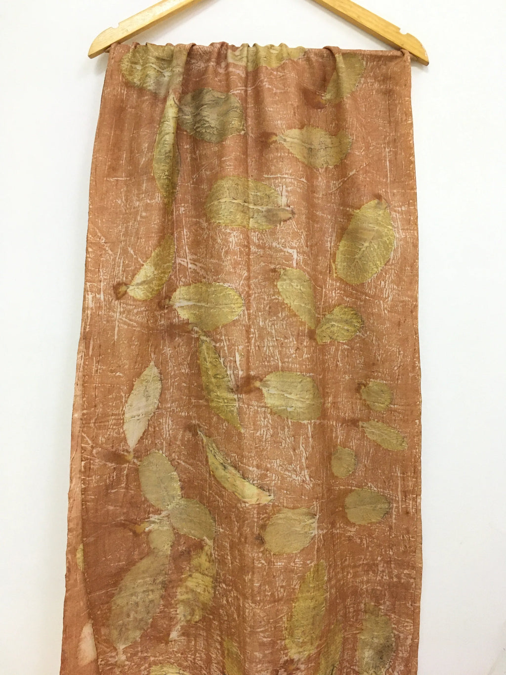 Brown pure silk scarf with green leaf pattern hanging on a wooden rod against a white background