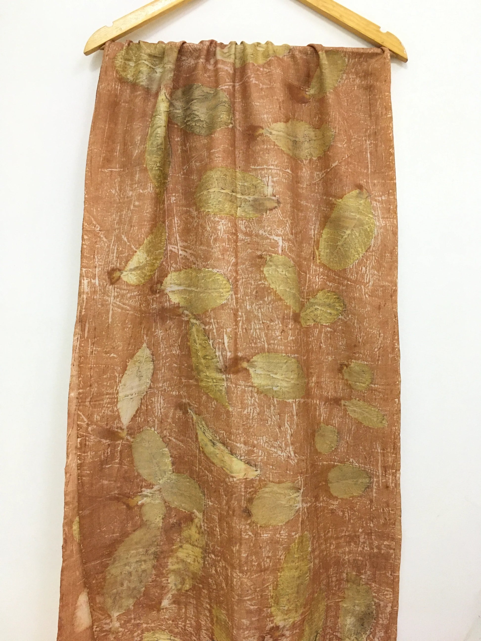 Brown pure silk scarf with green leaf pattern hanging on a wooden rod against a white background