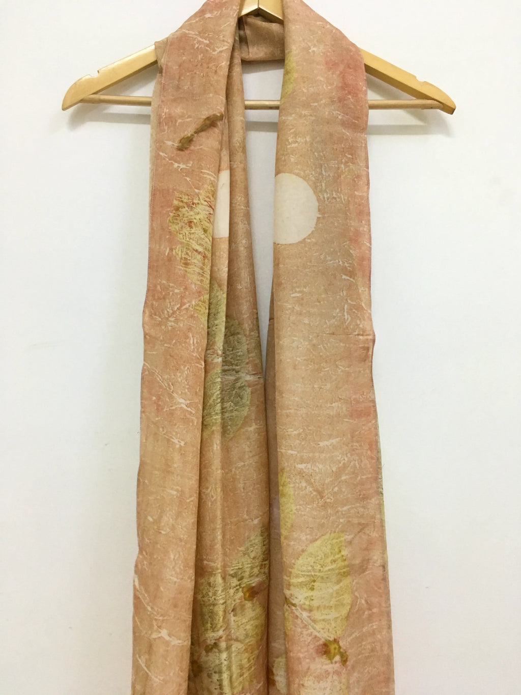 pure silk scarf featuring eco-printed guava leaves Scarf with nature-themed design on a wooden hanger against a white background