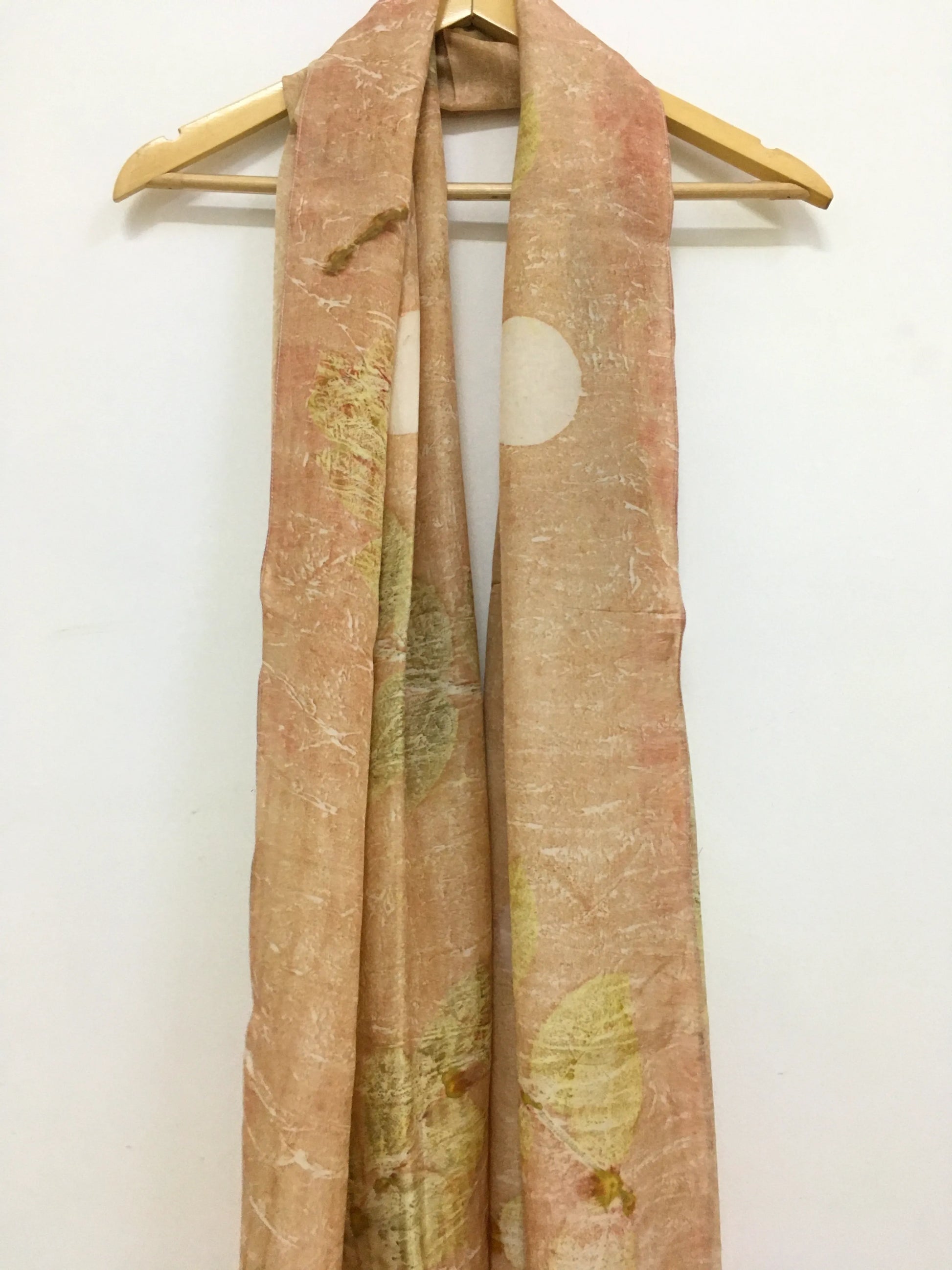 pure silk scarf featuring eco-printed guava leaves Scarf with nature-themed design on a wooden hanger against a white background
