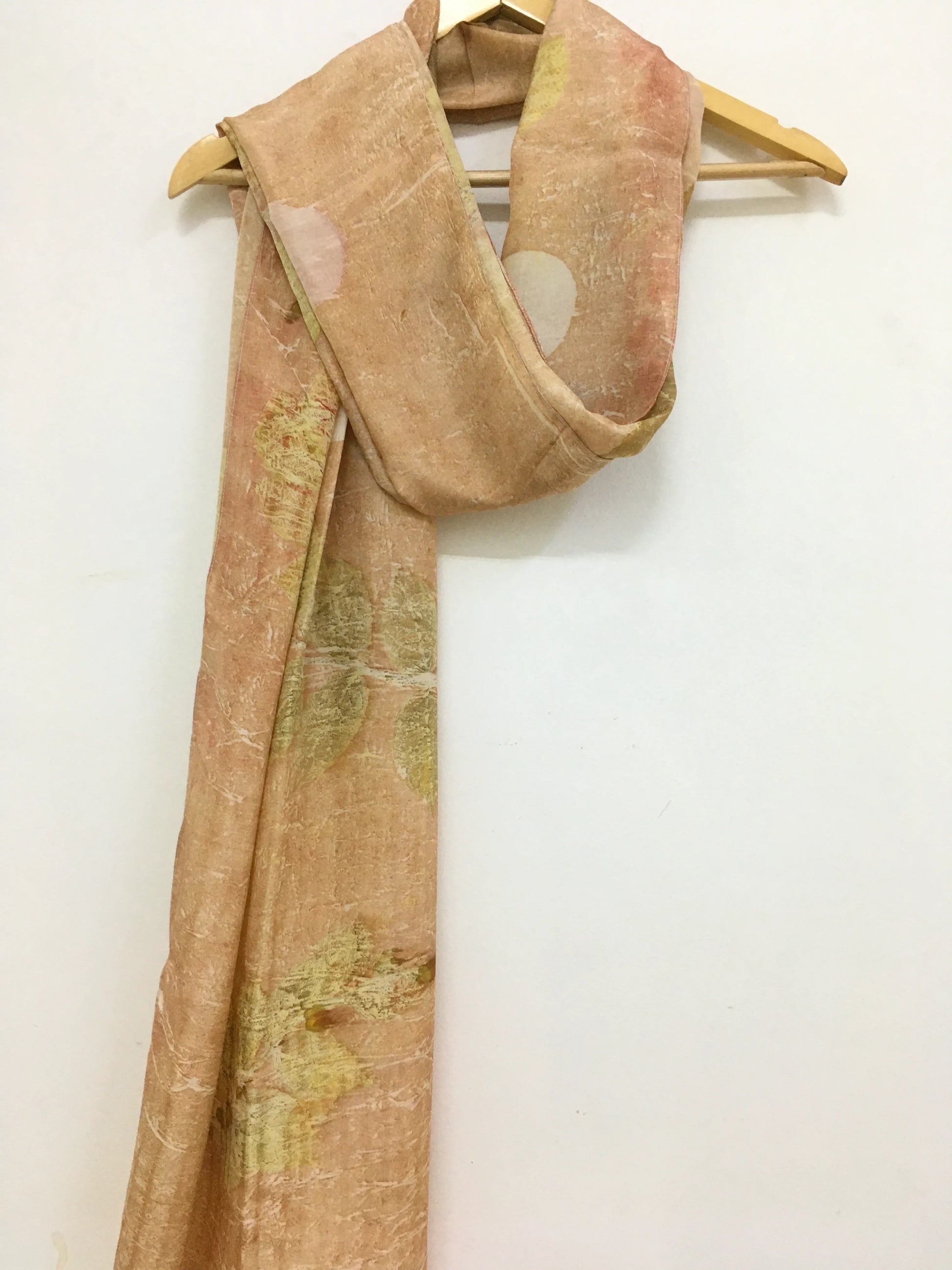 pure silk scarf featuring eco-printed guava leaves with a subtle pattern on a wooden hanger against a white background