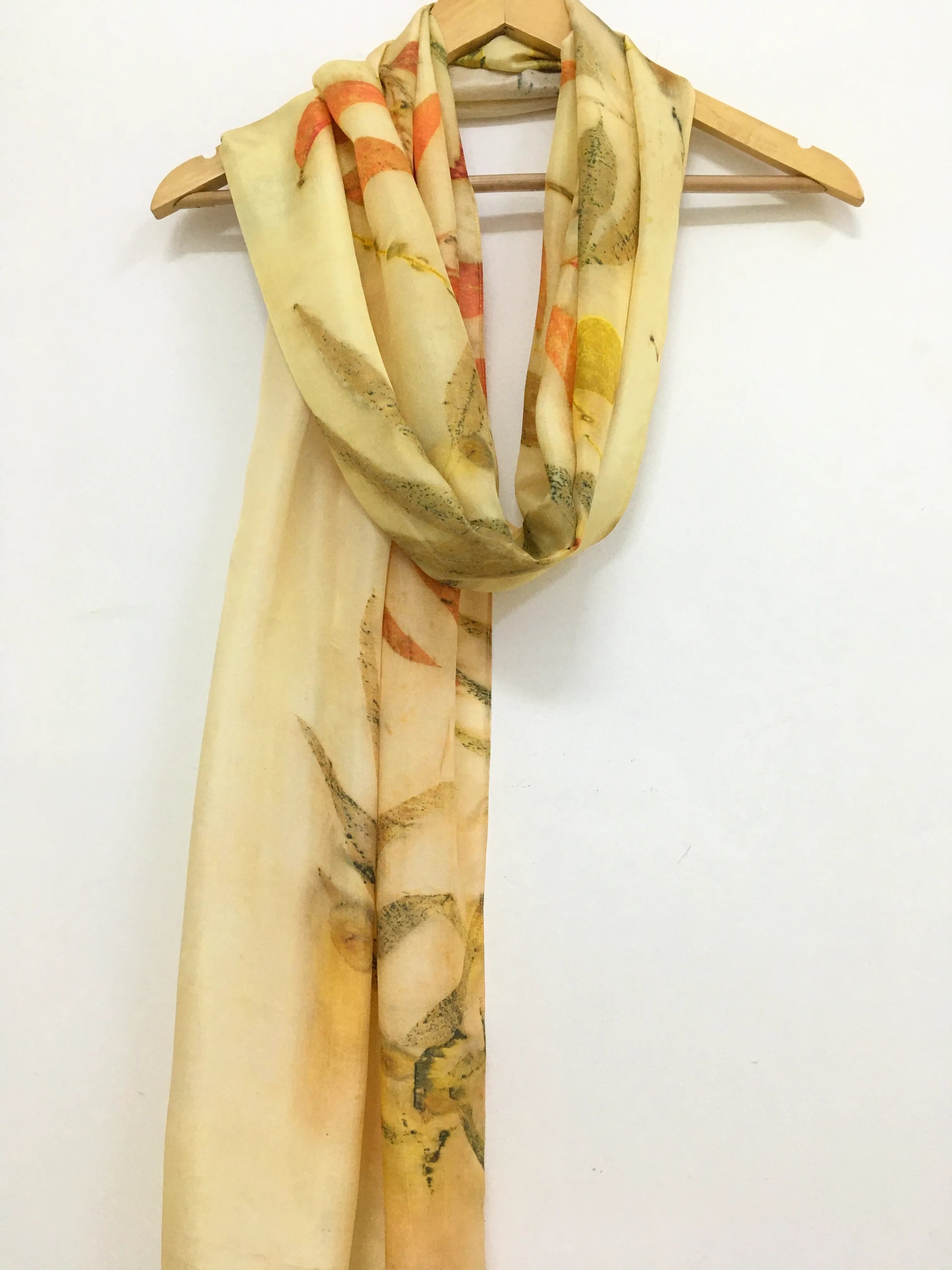 Golden Eucalyptus Eco Printed Pure Silk Scarf draped over a wooden hanger on a white background