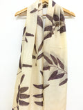 Beige Logwood Eucalyptus Eco Printed Pure Silk scarf with leaf pattern on a wooden hanger against a white background