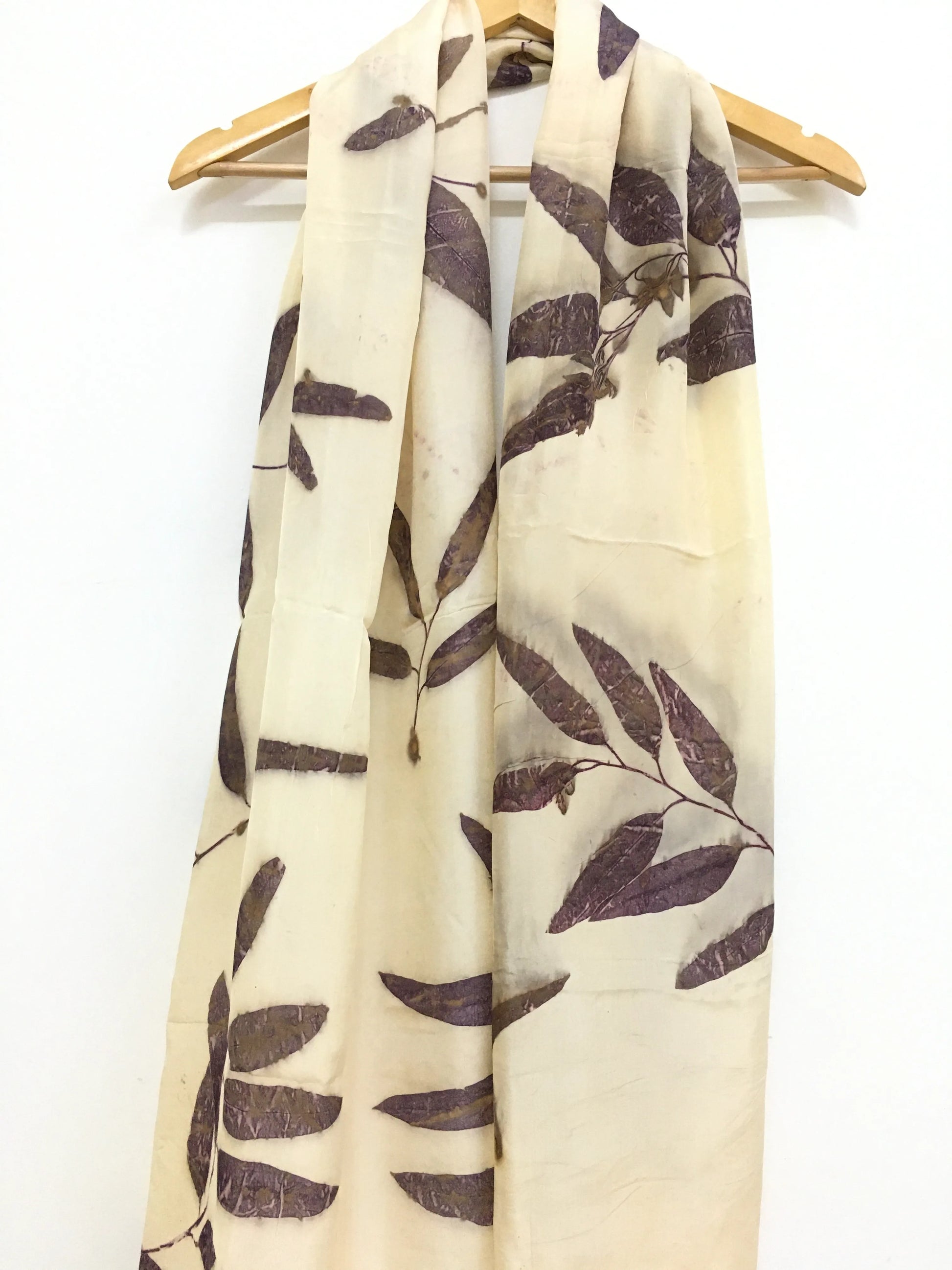 Beige Logwood Eucalyptus Eco Printed Pure Silk scarf with leaf pattern on a wooden hanger against a white background
