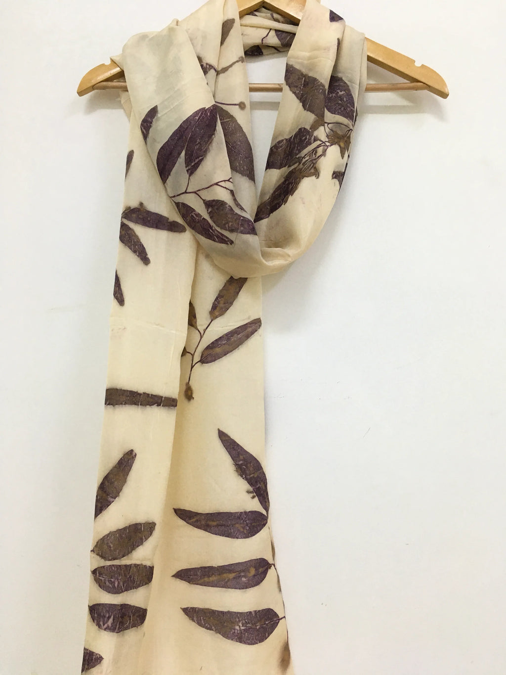 Beige Logwood Eucalyptus Eco Printed Pure Silk Scarf with leaf pattern on a wooden hanger against a white background
