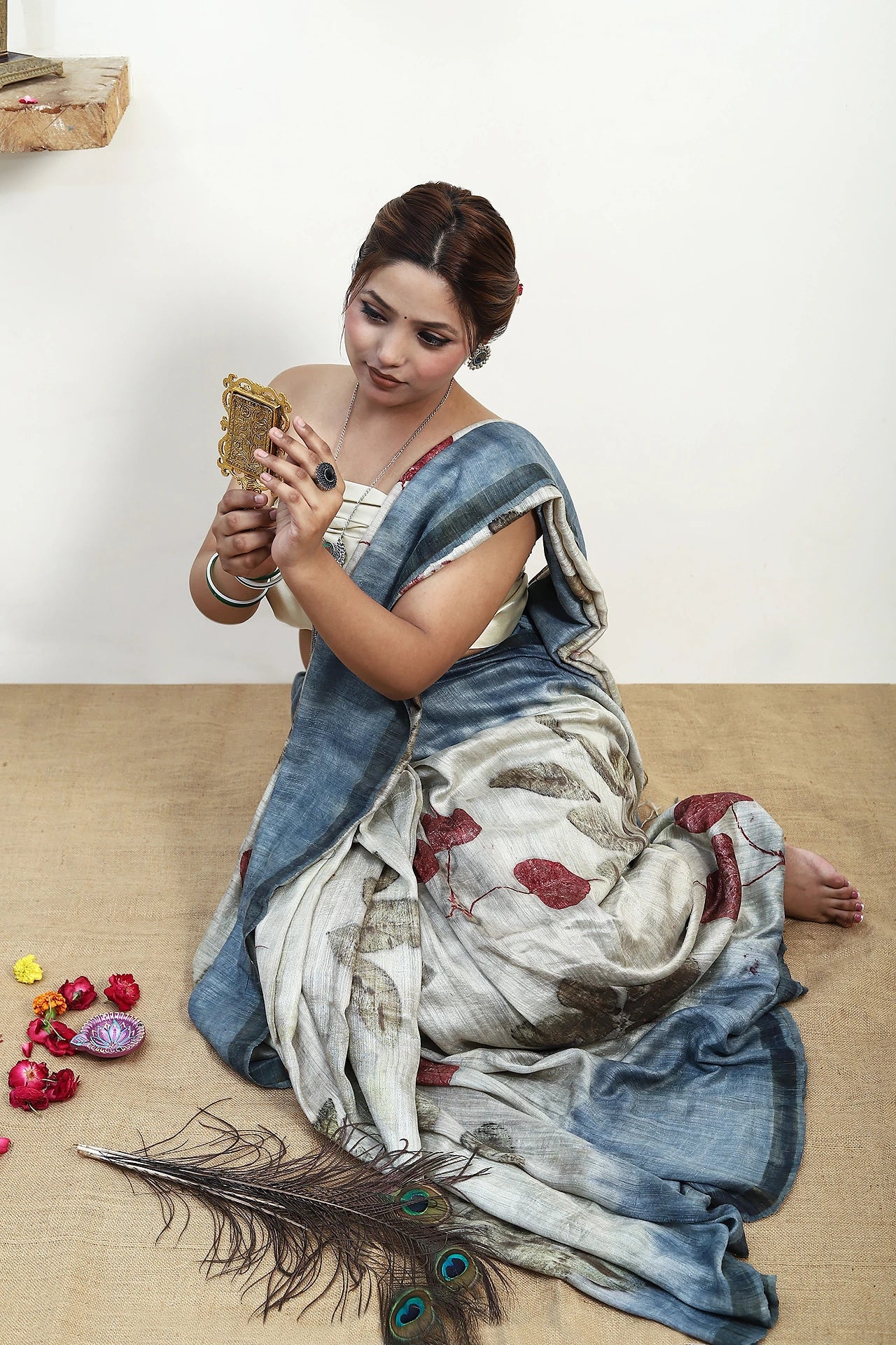Woman in a pure matka silk ecoprinted saree outfit sitting on the floor with a phone, surrounded by decorative items.