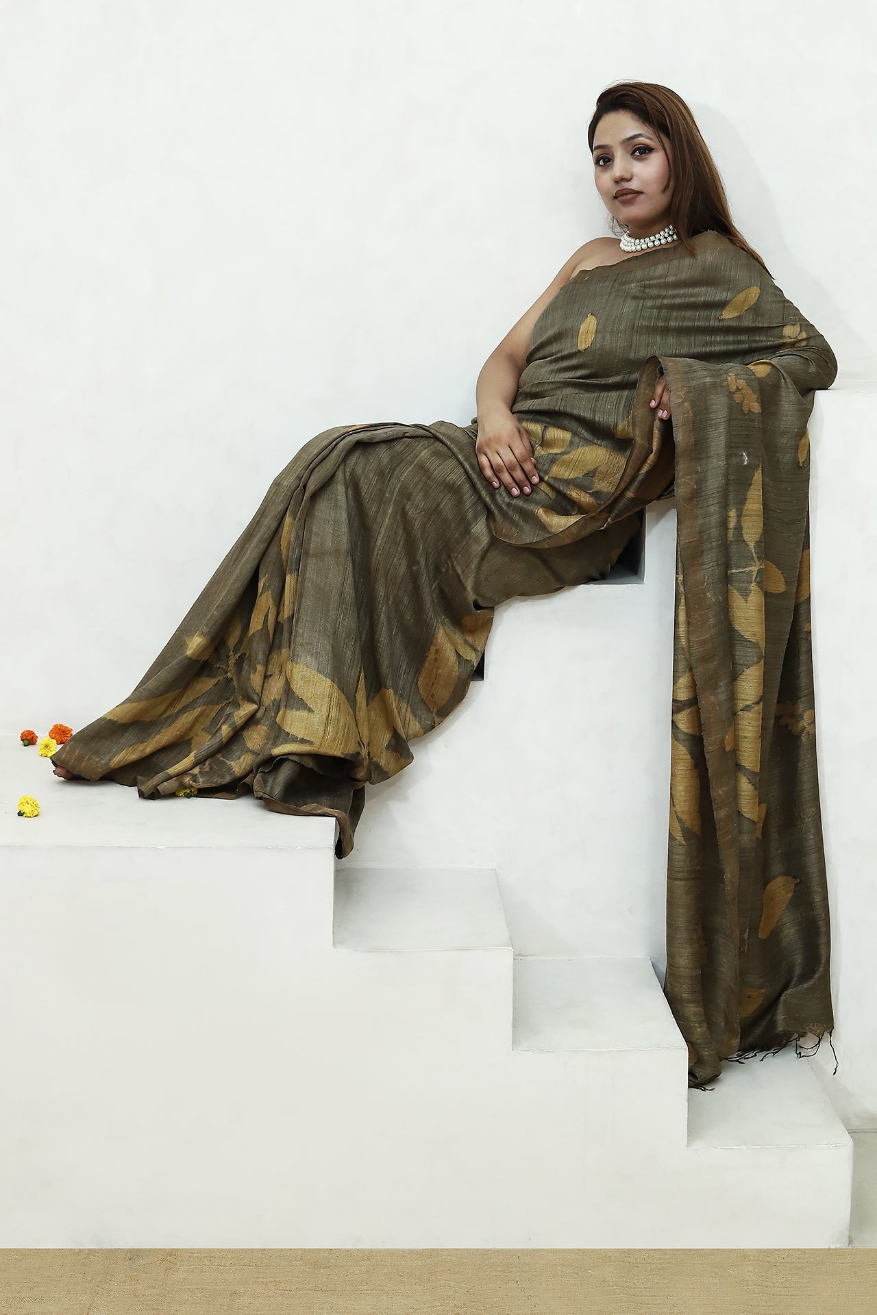 Woman in a green jamun ecoprinted pure matka silk saree sitting on white steps.