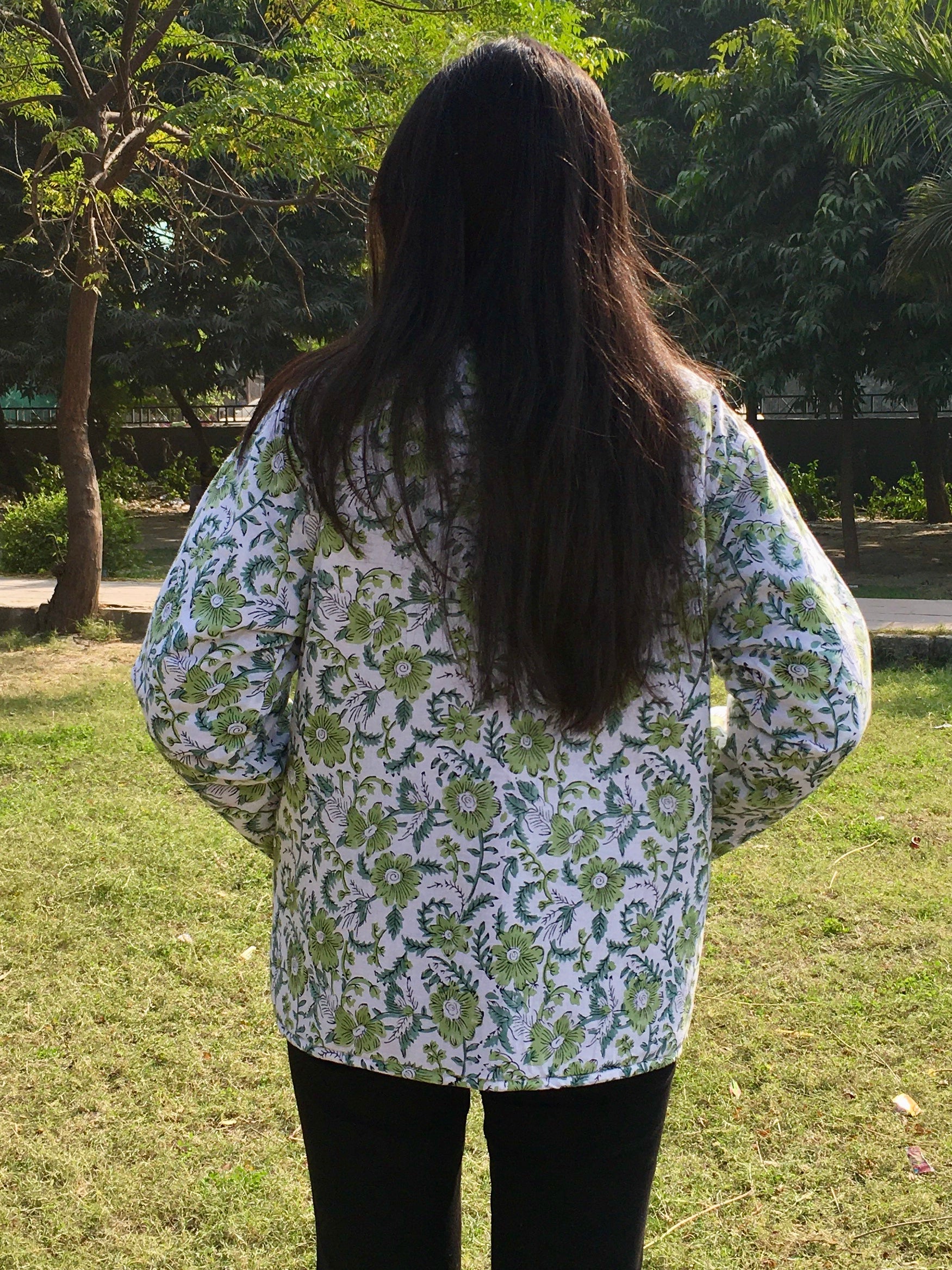 Person wearing a floral patterned reversible jacket standing outdoors with trees in the background