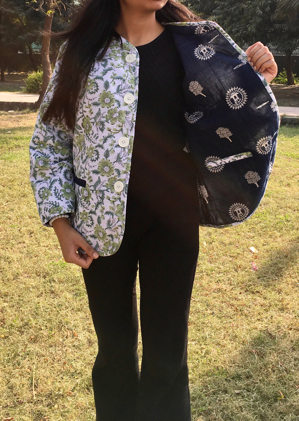 Person holding a dark blue reversible jacket outdoors on grass