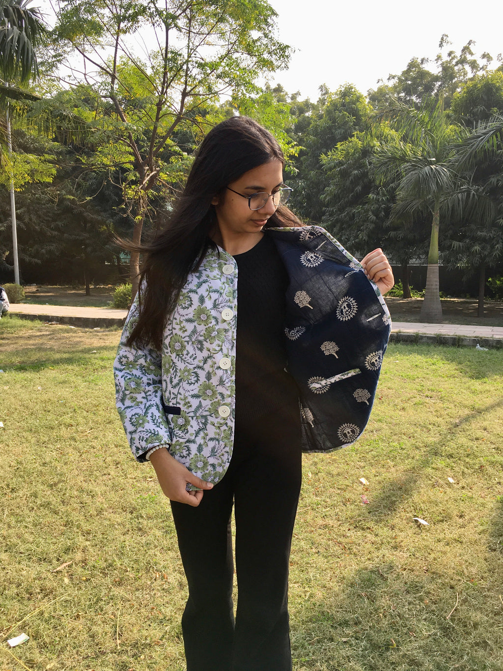 Person holding a double sided reversible jacket outdoors with greenery in the background