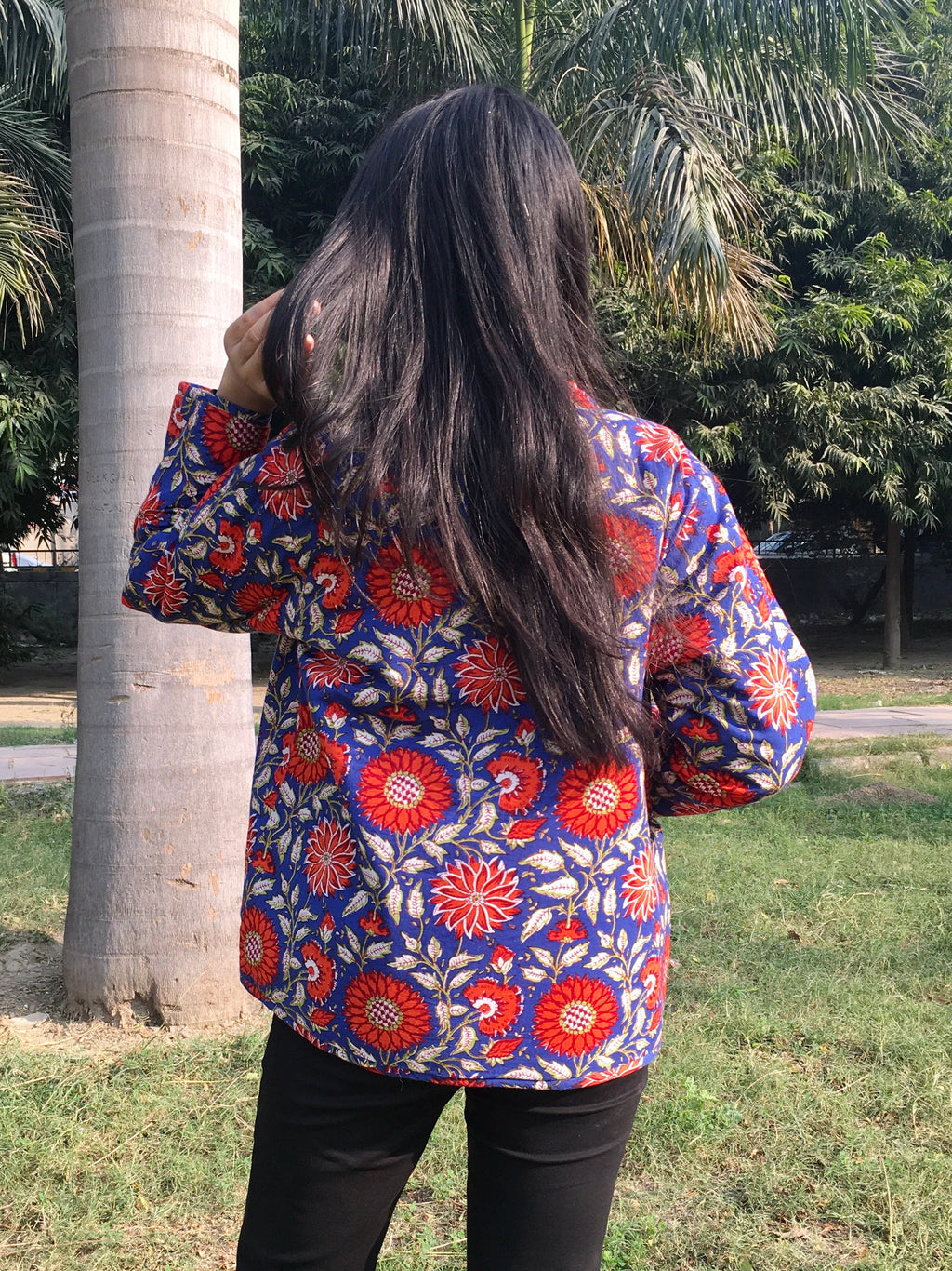Person wearing a colorful floral reversible jacket in an outdoor setting with trees and grass.