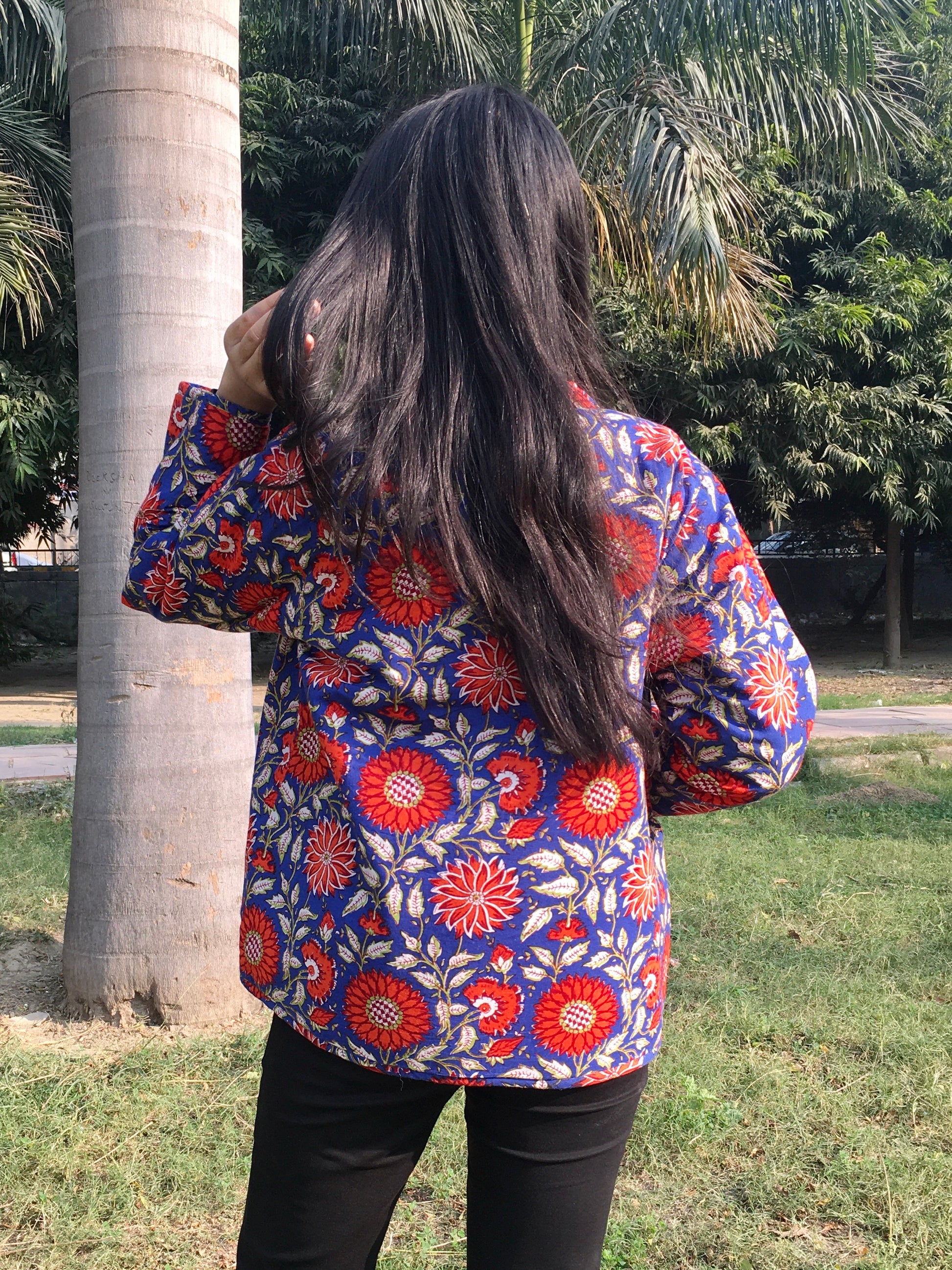 Person wearing a colorful floral reversible jacket in an outdoor setting with trees and grass.