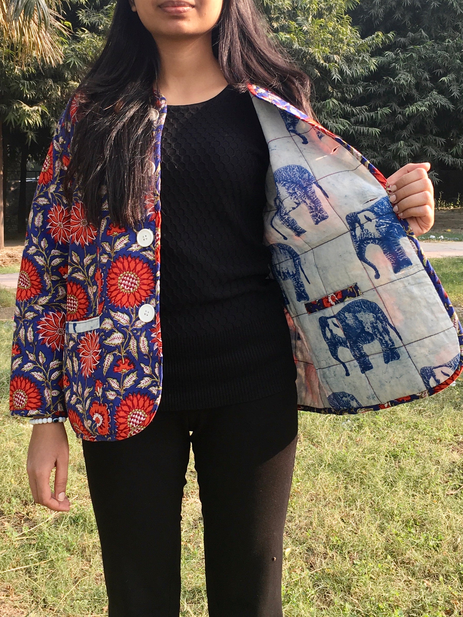 Person wearing a colorful quilted reversible jacketwith floral and elephant patterns outdoors.