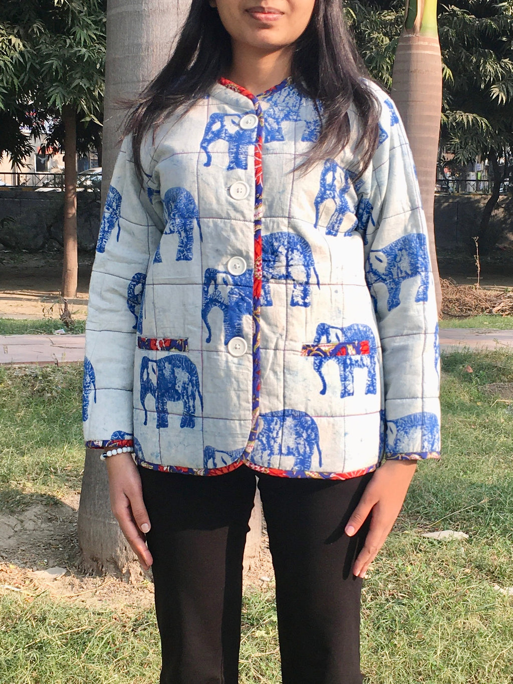 Person wearing a quilted reversible jacket with blue elephant patterns outdoors.