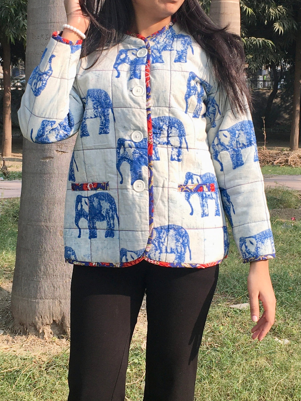 women wearing a blue and white quilted reversible jacket with elephant patterns outdoors.