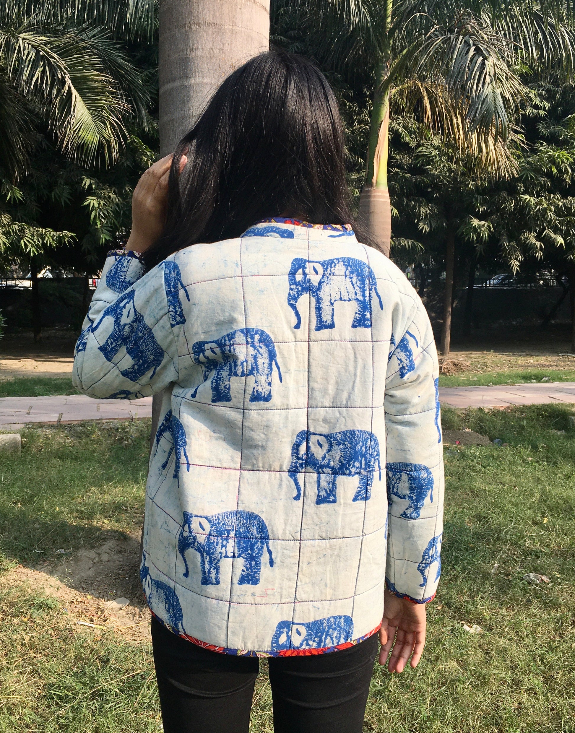 women wearing a quilted reversible jacket with blue elephant patterns outdoors.