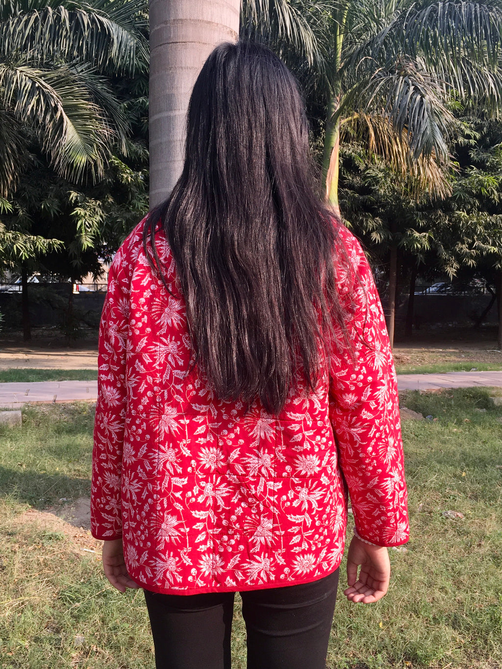 women wearing a red floral reversible jacket standing in a park with palm trees.