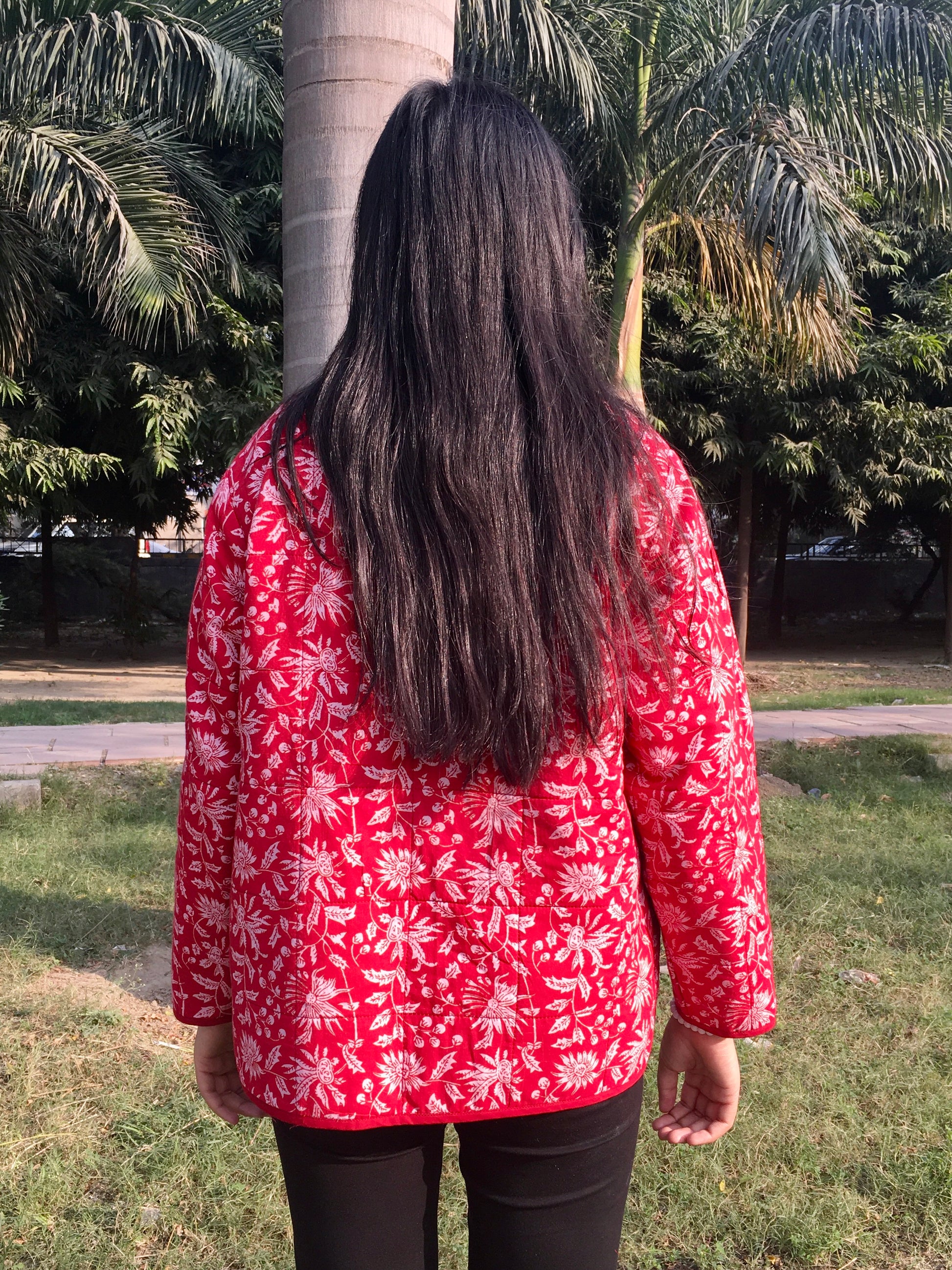 women wearing a red floral reversible jacket standing in a park with palm trees.