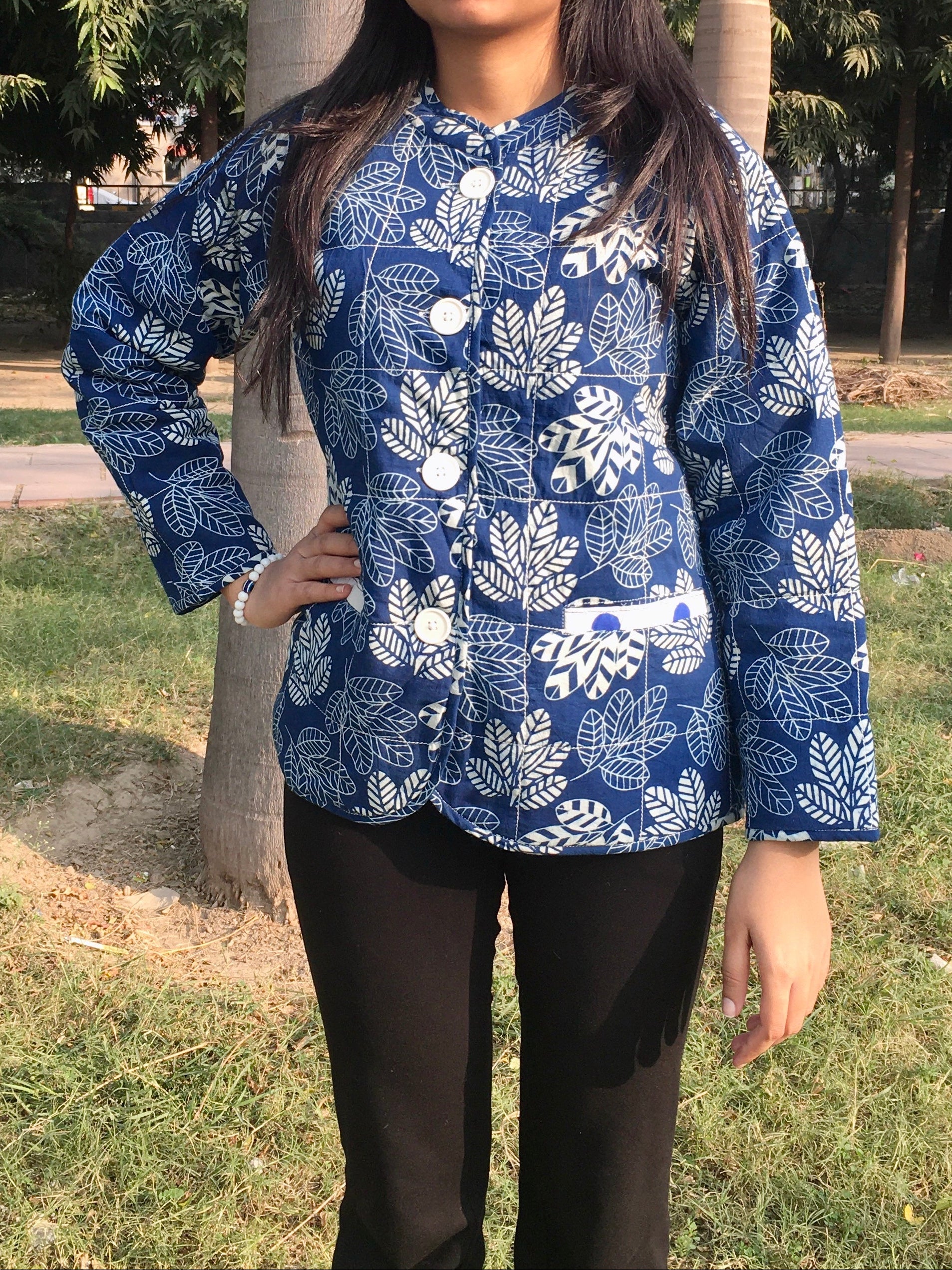 Woman wearing a blue patterned reversible jacket outdoors with trees in the background