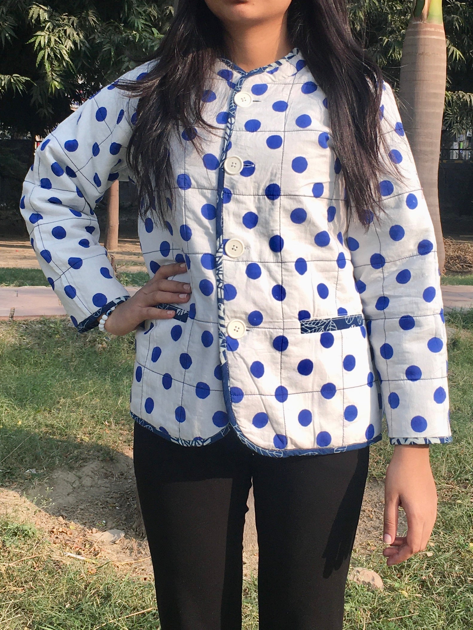 women wearing a white quilted reversible jacket with blue polka dots outdoors.