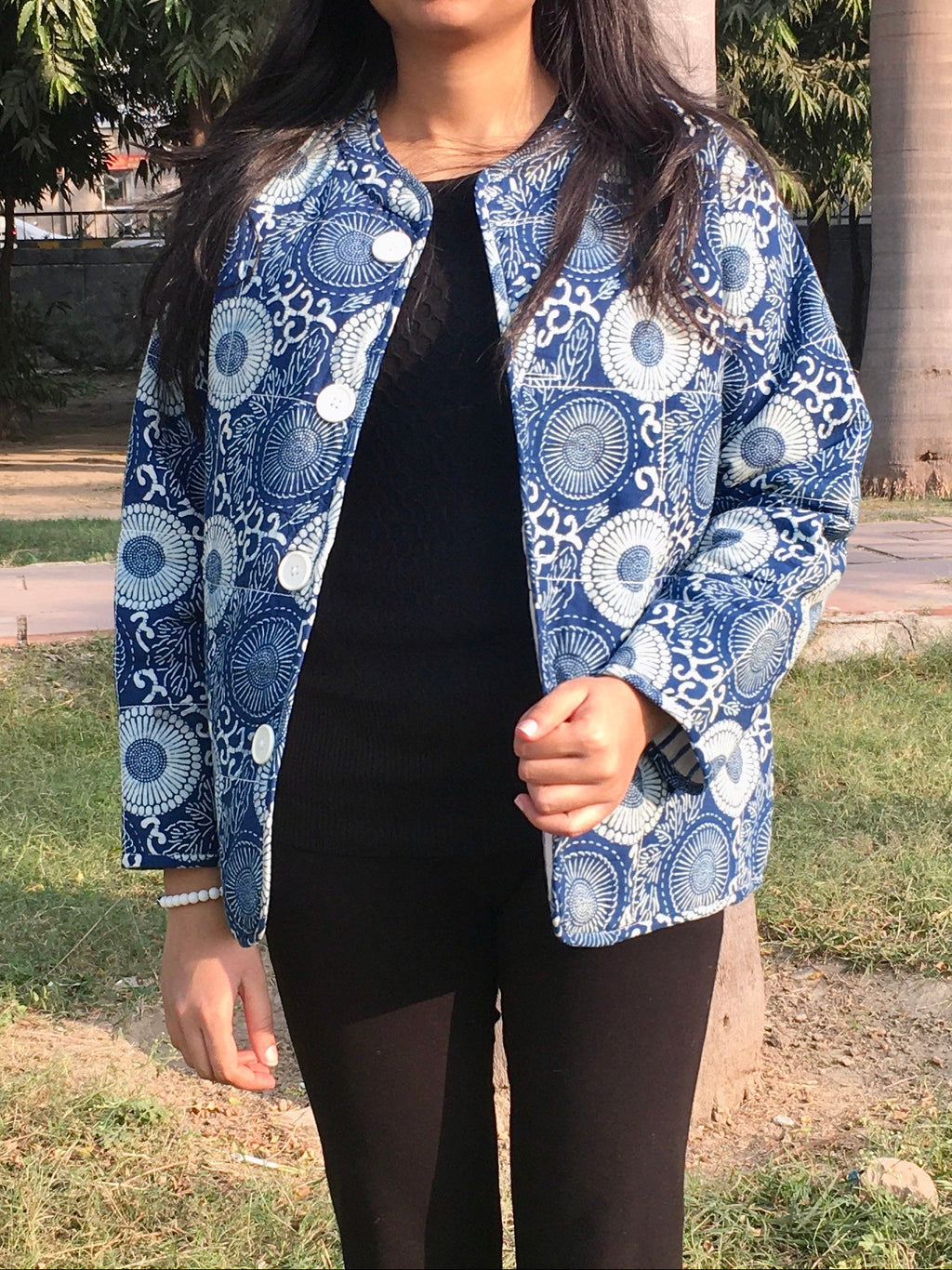 Woman wearing a blue patterned reversible jacket outdoors with trees in the background