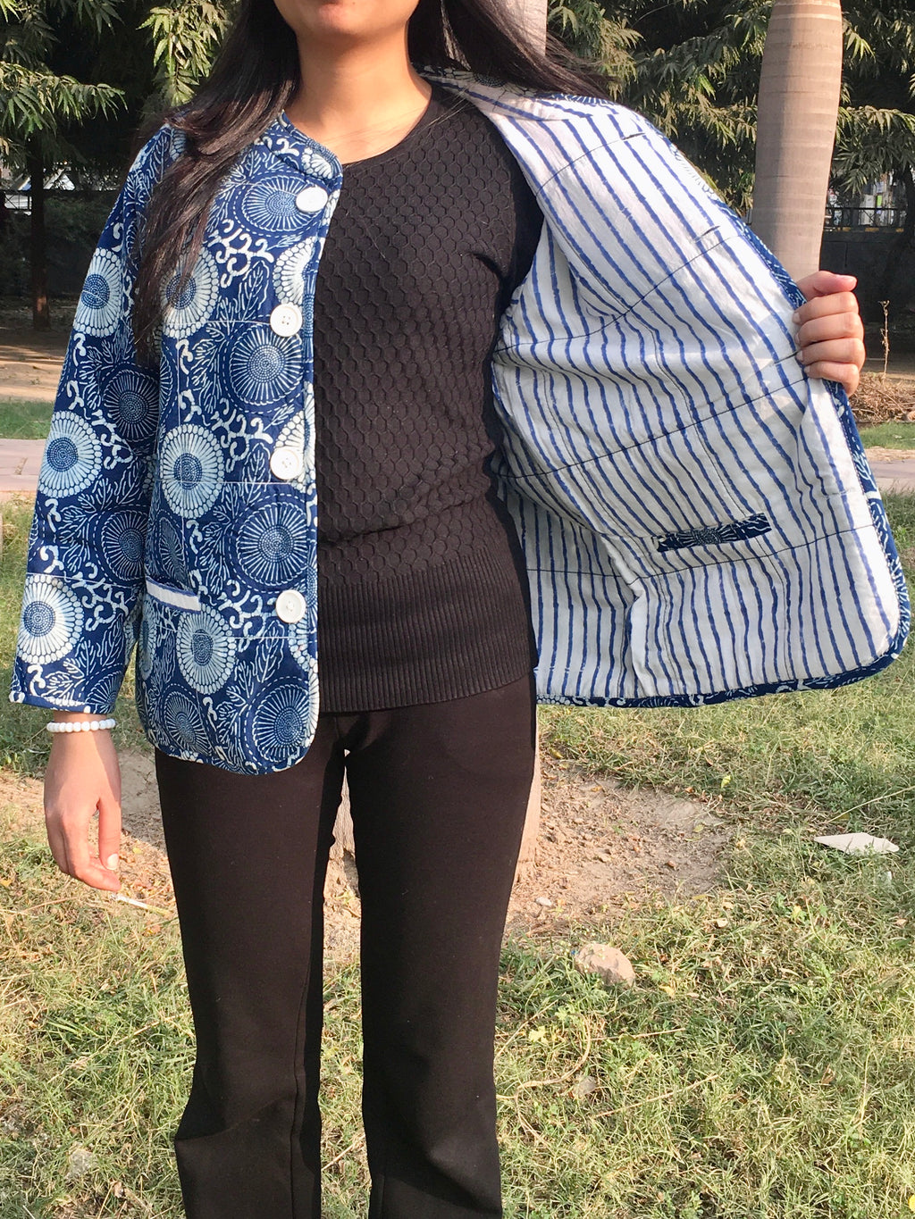 Person wearing a blue and white patterned reversible jacket over a black sweater and pants outdoors.