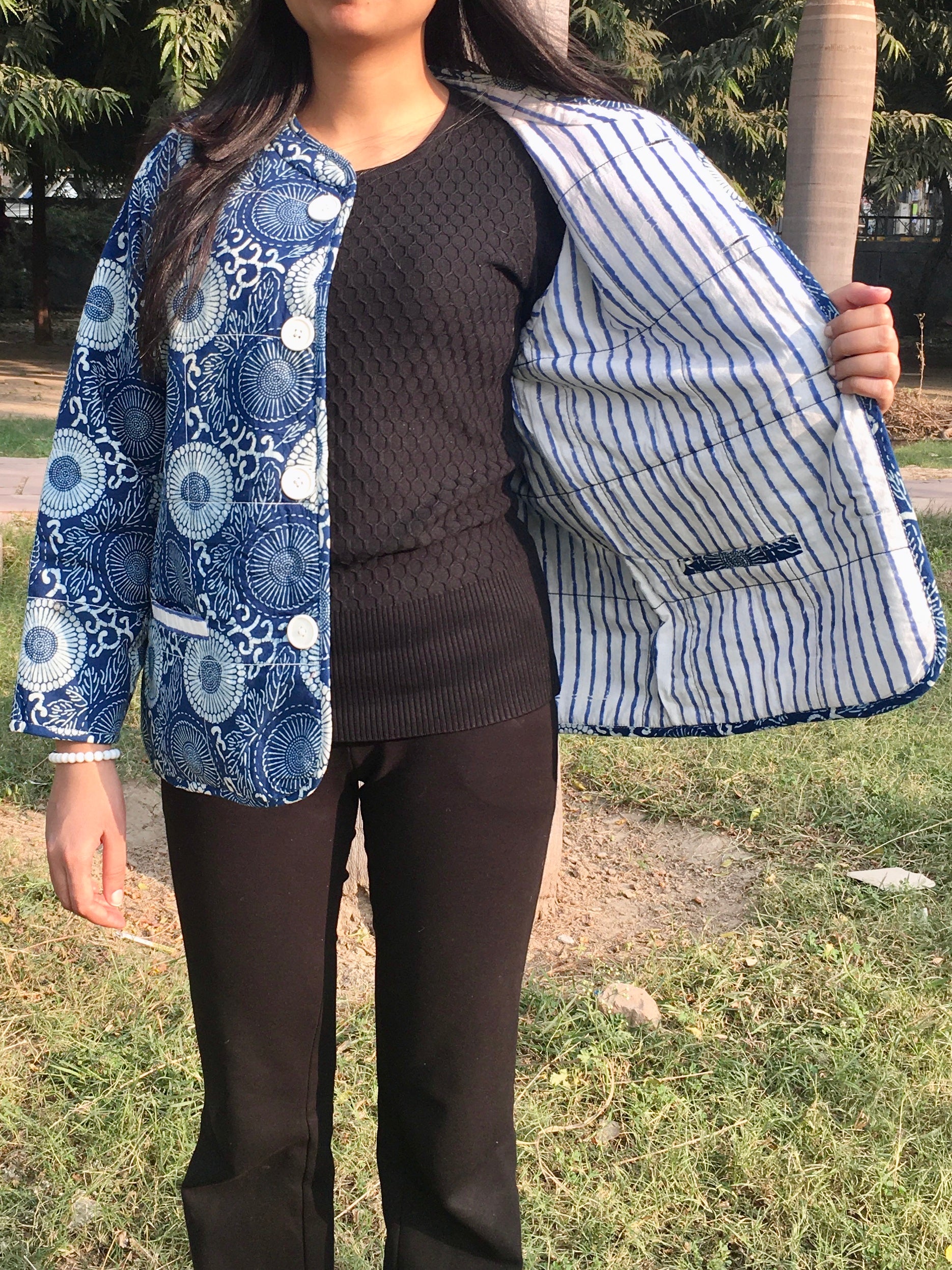 Person wearing a blue and white patterned reversible jacket over a black sweater and pants outdoors.
