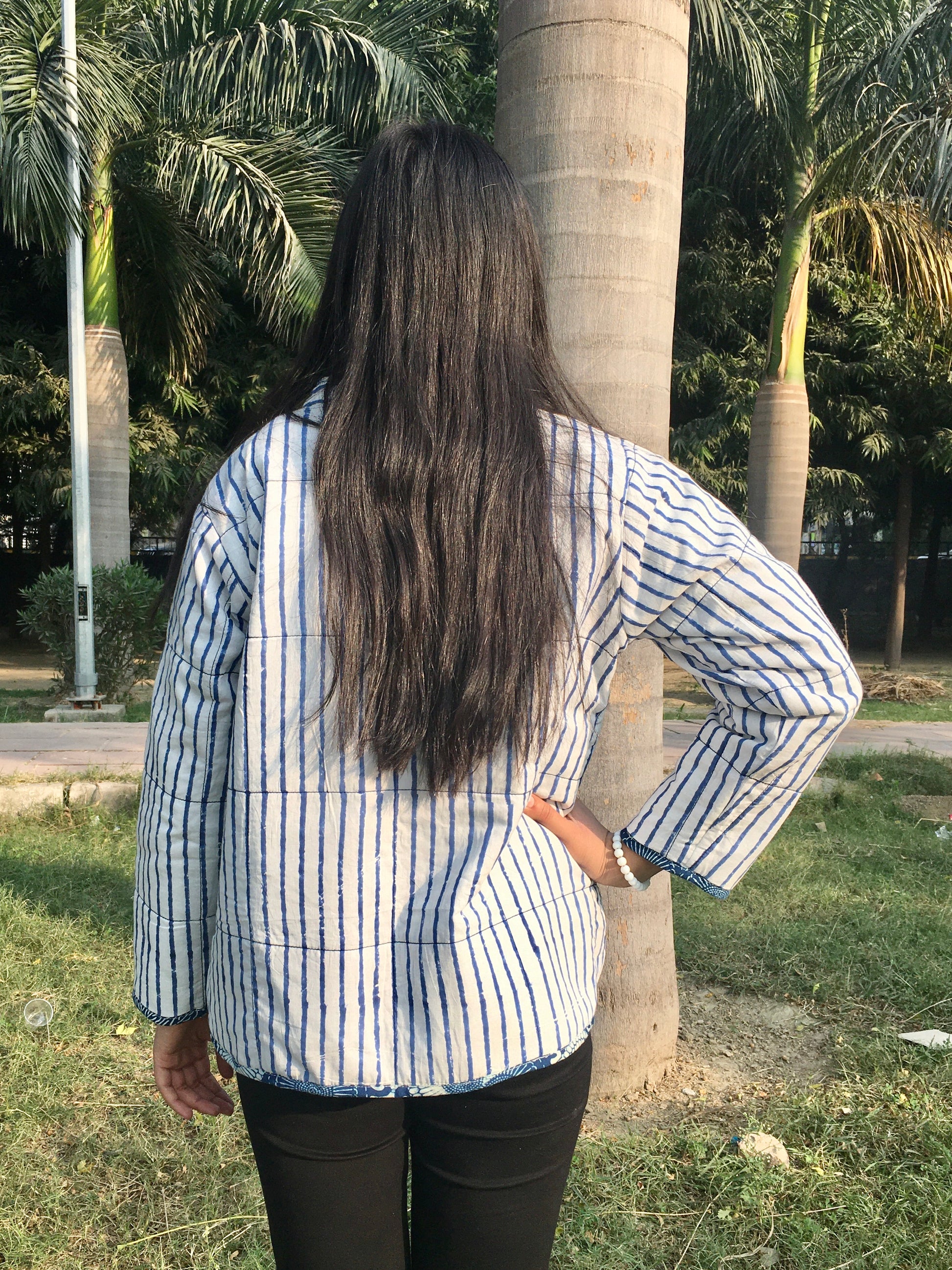 women wearing a blue and white striped reversible jacket standing outdoors with trees in the background