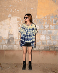 girl wearing a tie dye Kaftan Flared Top and black shorts standing against a textured wall.