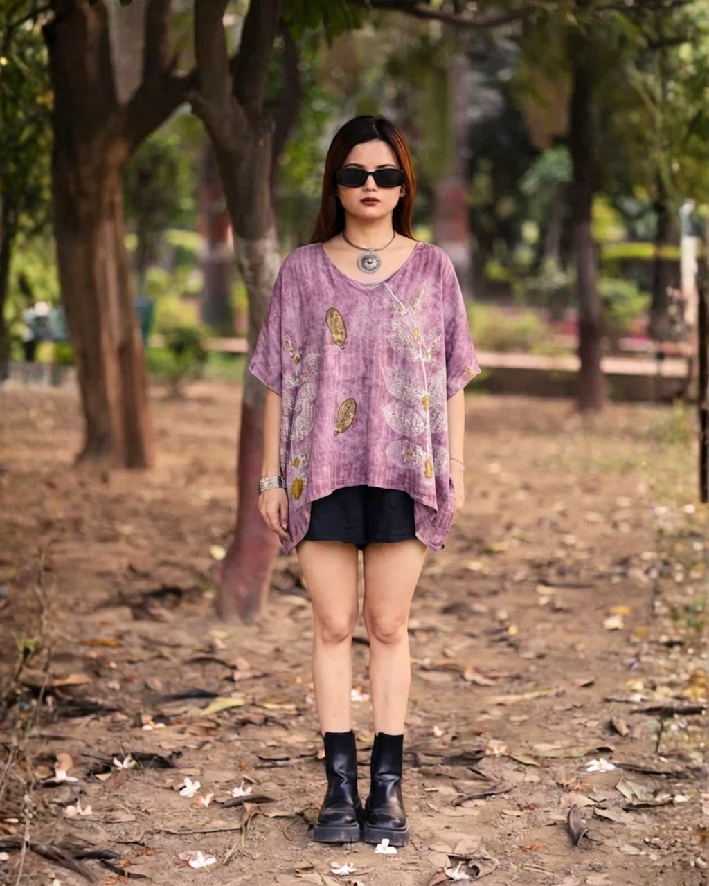 Woman wearing a purple Kaftan Flared Top and black shorts standing in a park.