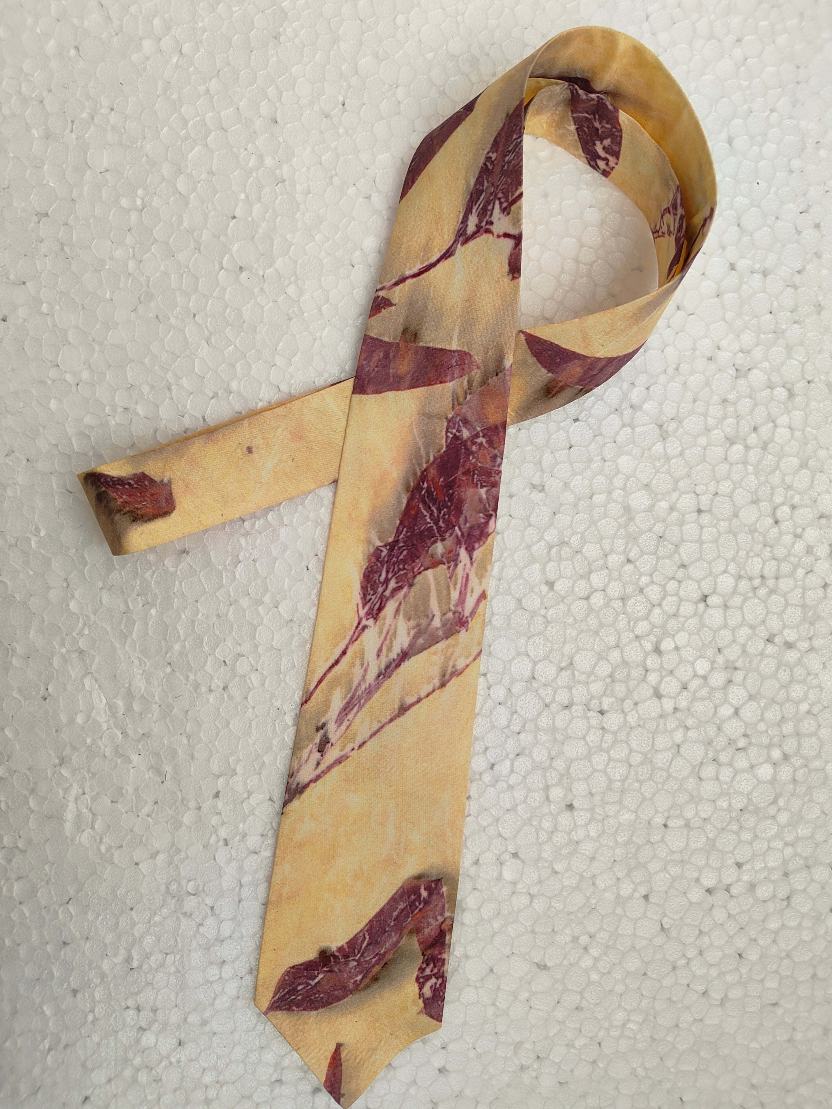 Maroon and beige patterned tie on a textured white background