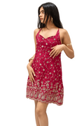 A woman modeling a short magenta pink sleeveless mini dress with intricate gold floral embroidery and a scalloped lace hem, posed against a draped white fabric backdrop.