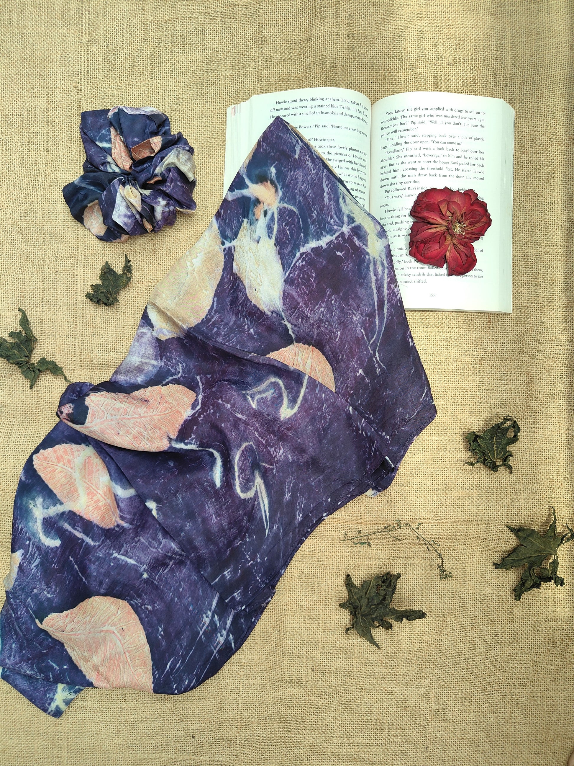 Ecoprinted Scarf with floral design on a textured surface with an open book and dried flowers.